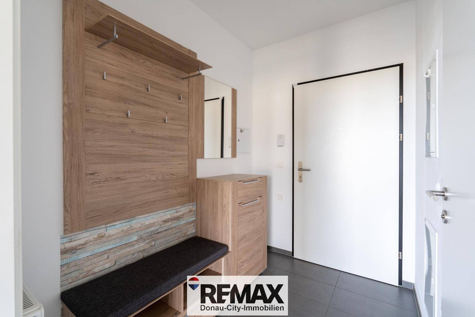 Heller Eingangsbereich mit moderner Garderobe aus Holz und dunklen Bodenfliesen.