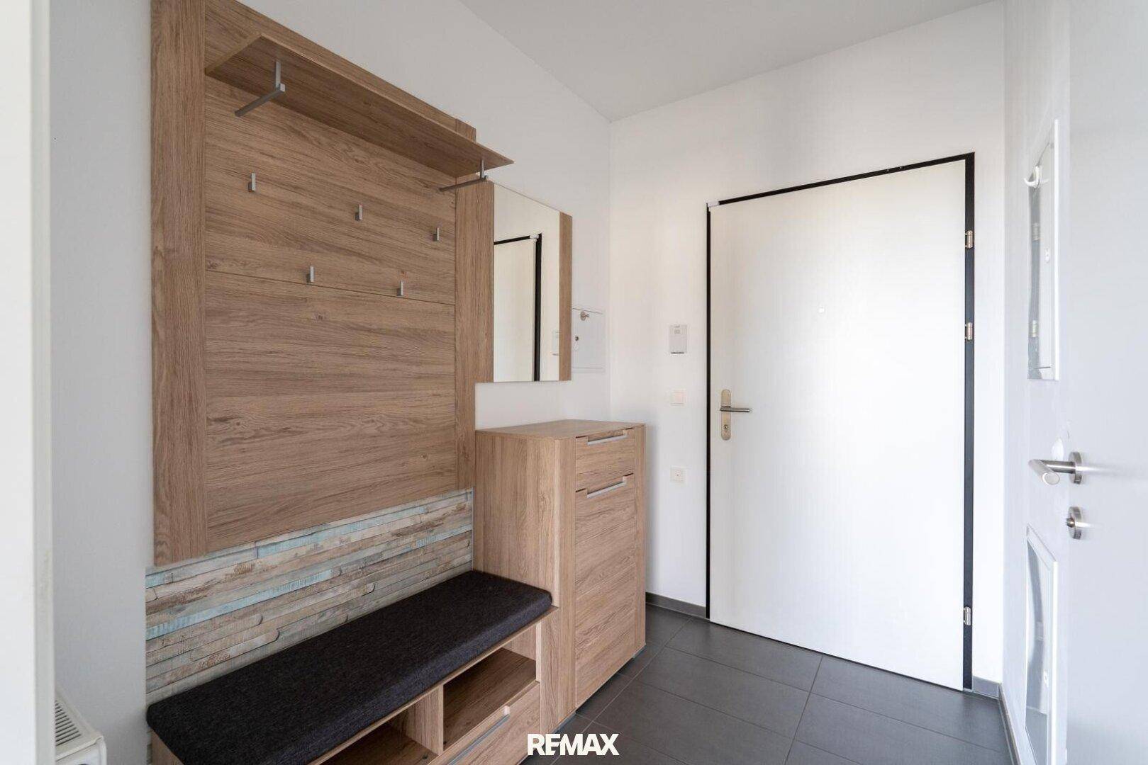 Heller Eingangsbereich mit Garderobe, Schuhschrank und Sitzbank auf dunklen Fliesen.