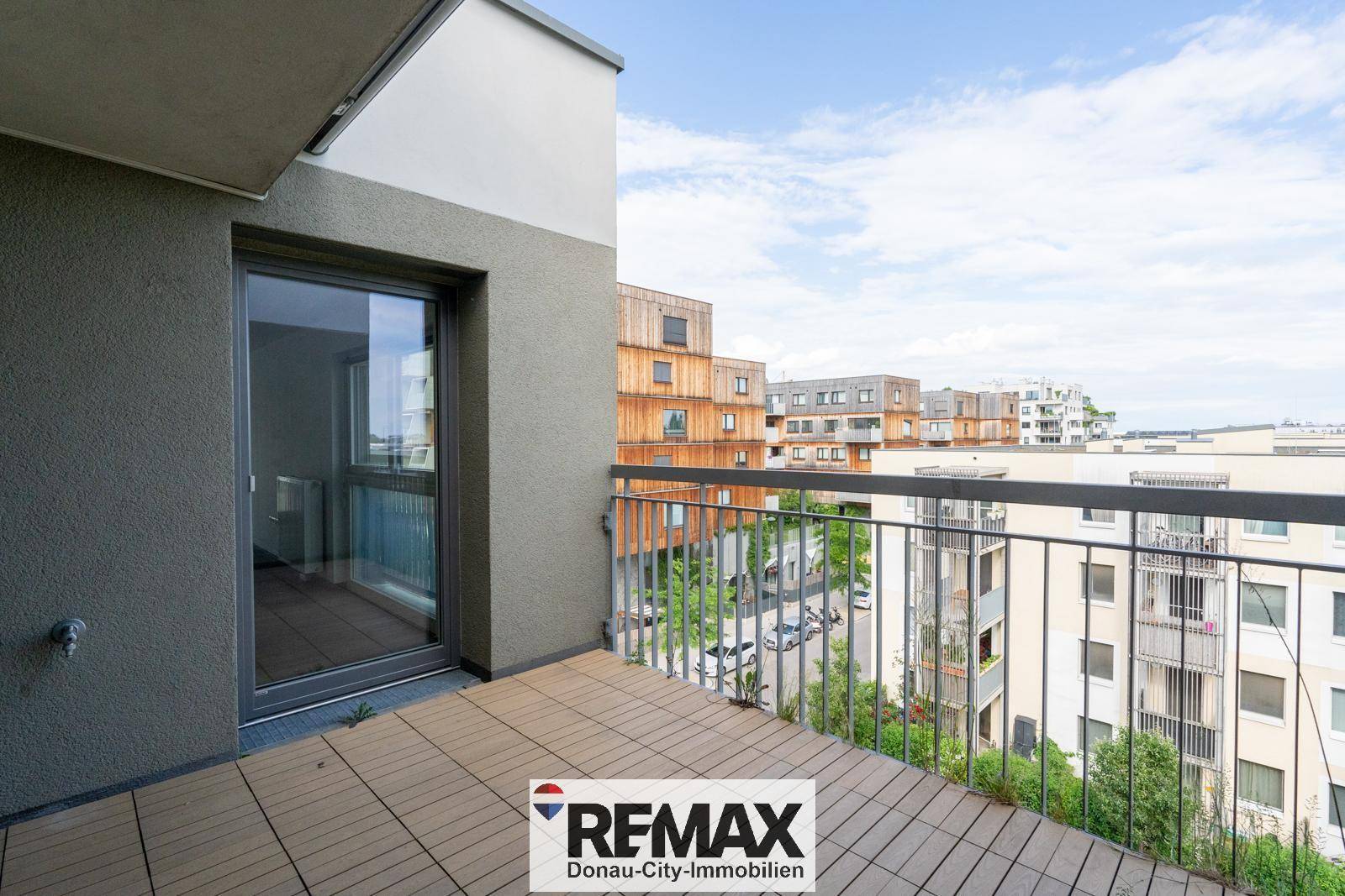 Heller Balkon mit Holzbodenfliesen und Zugang zum Innenraum, bietet einen weiten Blick.