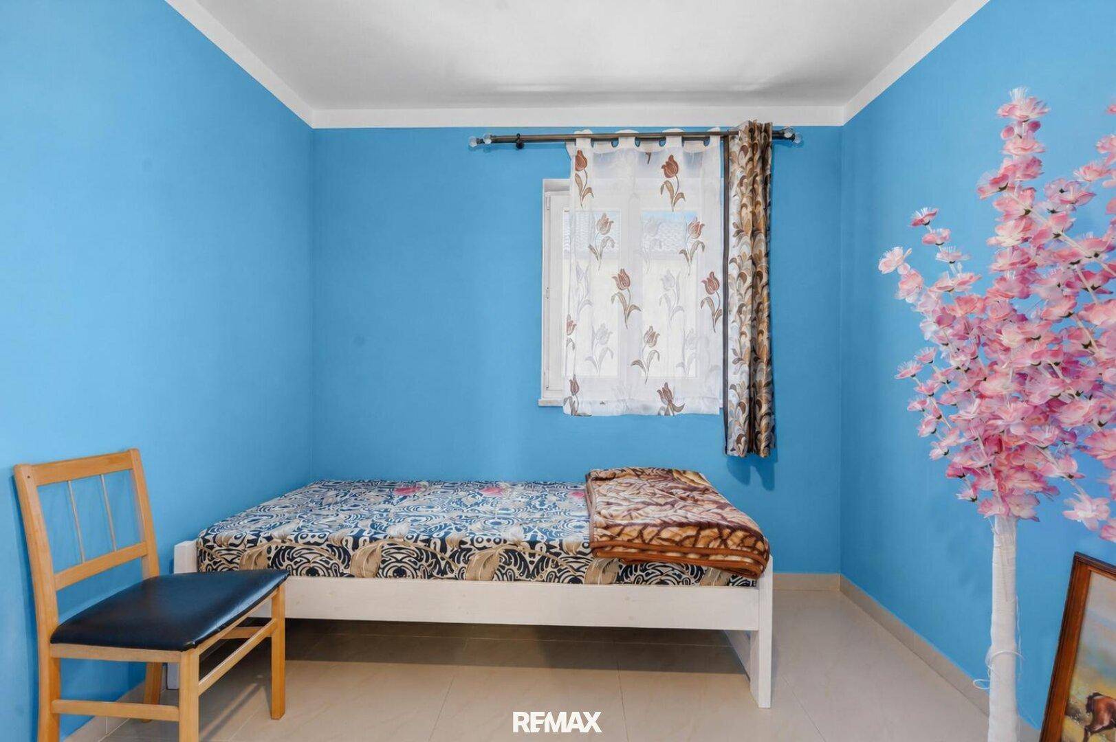 Schlafzimmer mit leuchtend blauen Wänden, Einzelbett und einem Fenster mit Vorhängen.