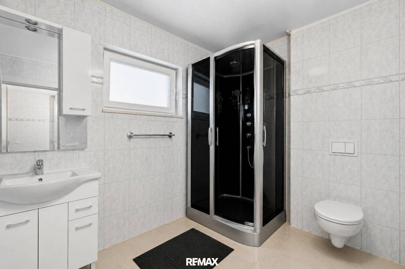 Badezimmer mit Duschkabine, WC, Waschbecken und hellen Fliesen an Wänden und Boden.