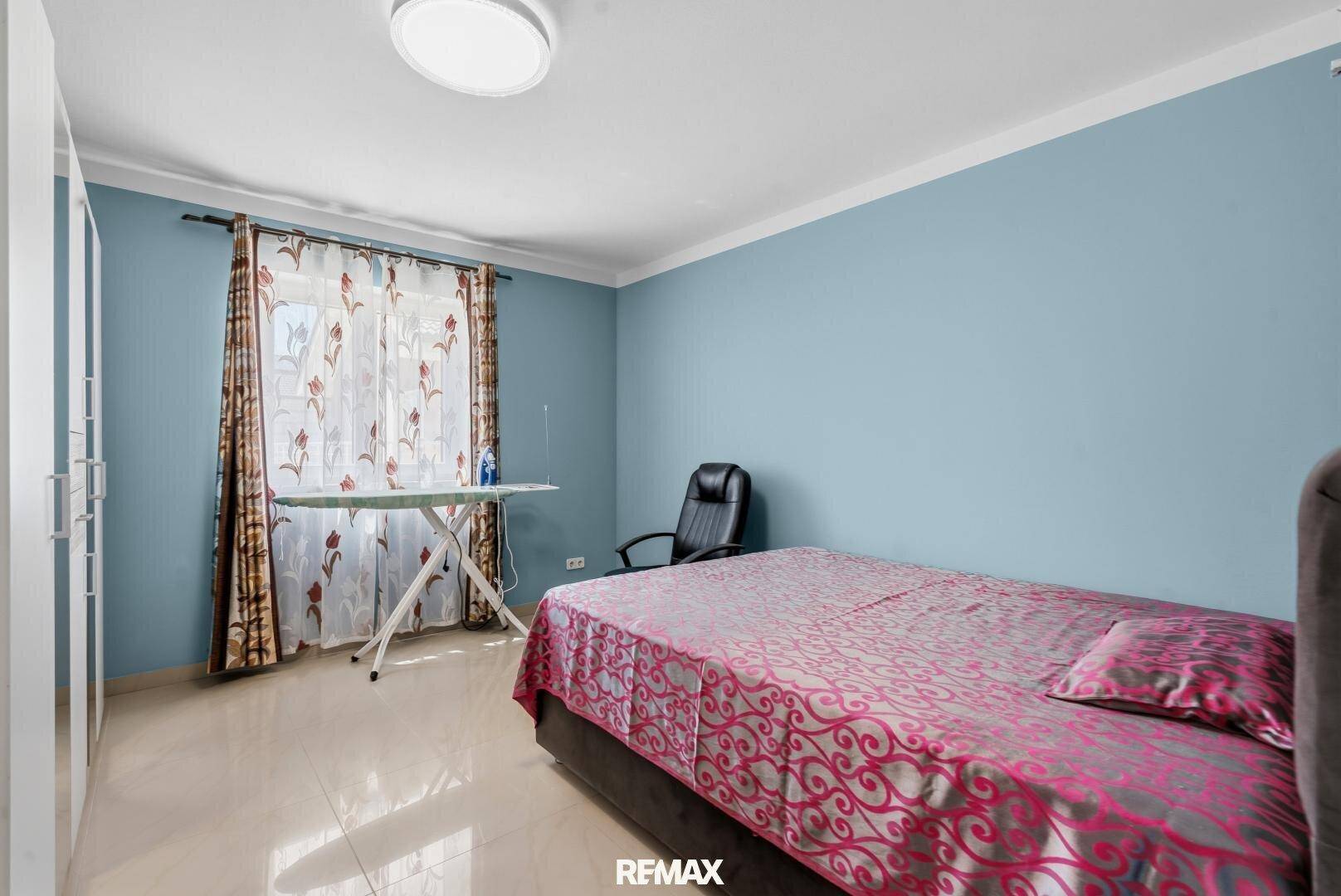 Schlafzimmer mit blau gestrichenen Wänden, Einzelbett und Bügelbrett am Fenster.