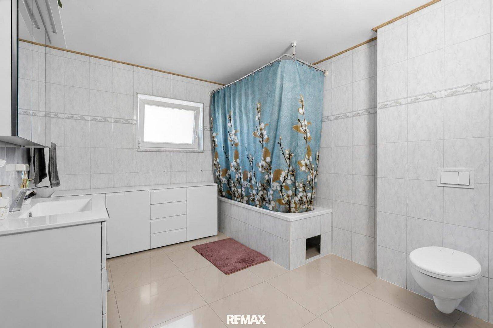 Badezimmer mit Badewanne, WC, Waschbecken und hellen Fliesen an Wänden und Boden.