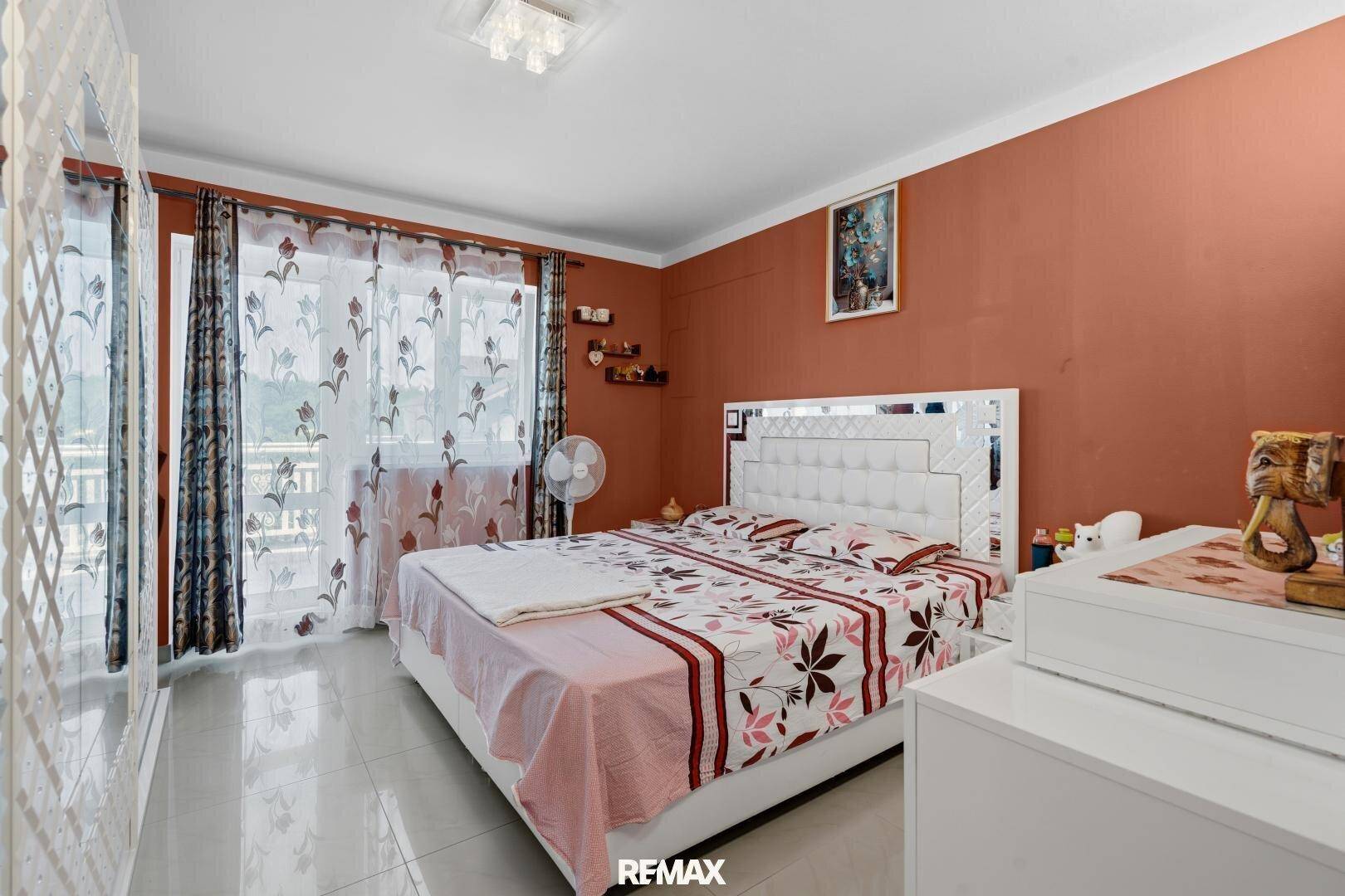 Geräumiges Schlafzimmer mit Doppelbett, orangefarbenen Wänden und Zugang zum Balkon.