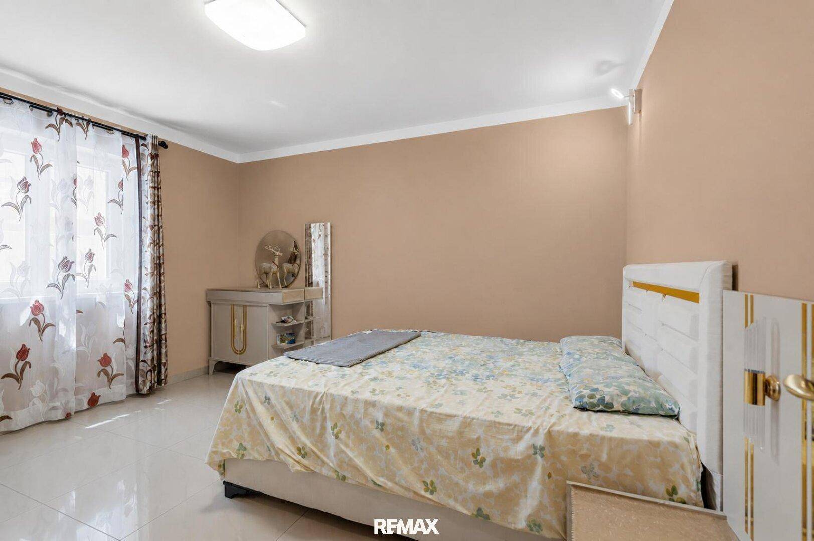 Helles Schlafzimmer mit Doppelbett, beigefarbenen Wänden und einem Schminktisch.