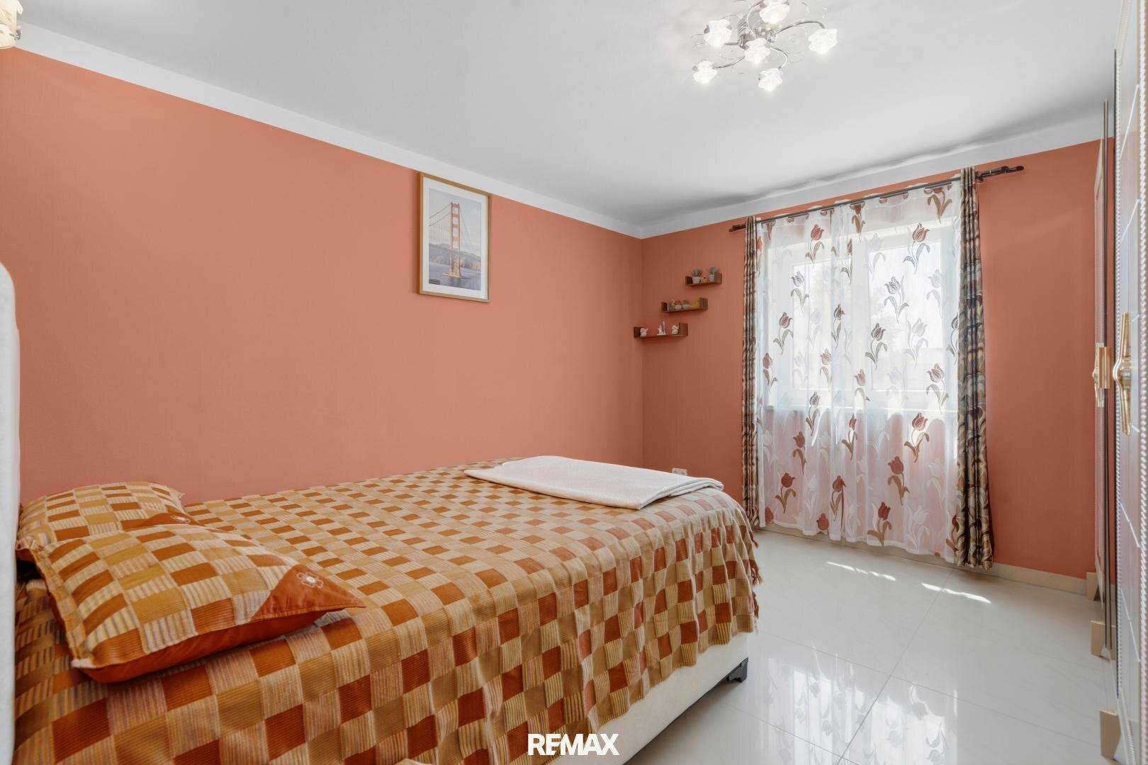 Schlafzimmer mit orangefarbenen Wänden, Einzelbett und einem Fenster mit gemusterten Vorhängen.