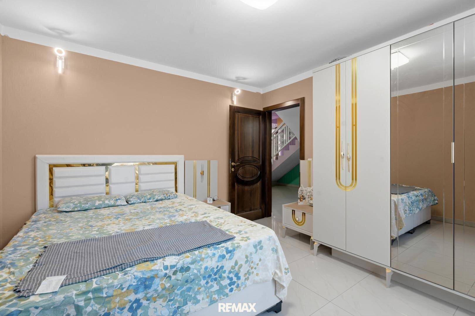 Schlafzimmer mit hellem Doppelbett, Spiegelschrank und beigefarbenen Wänden.