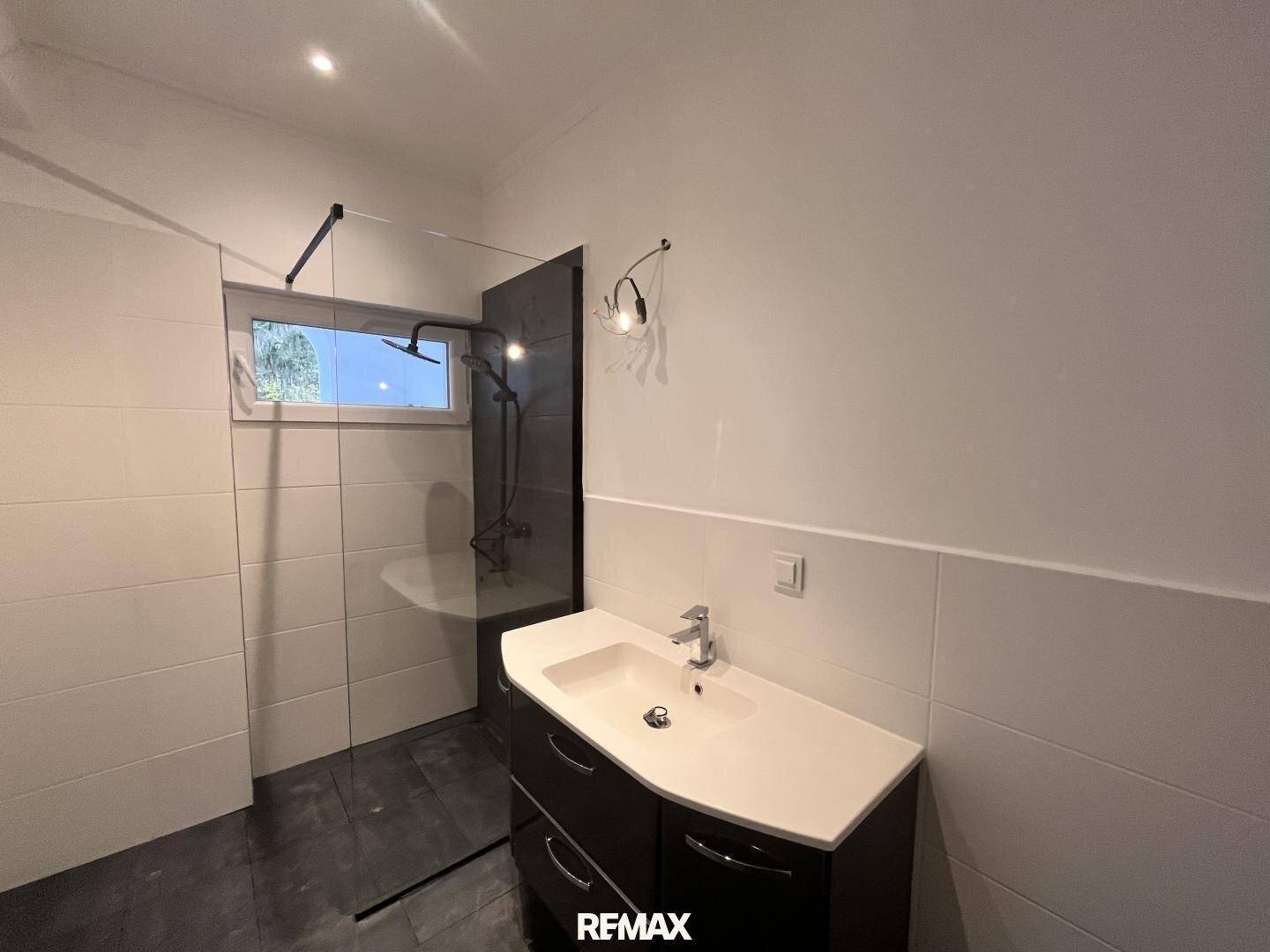 Modernes Badezimmer mit begehbarer Dusche, Waschtisch und Fenster für Tageslicht.