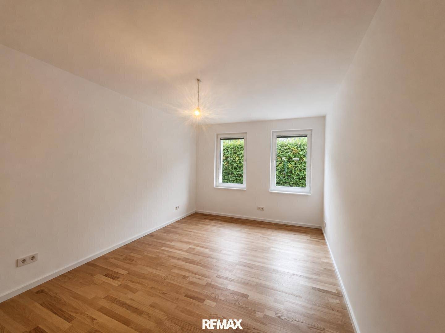 Geräumiges Schlafzimmer mit Holzparkettboden und zwei Fenstern mit Heckenblick.