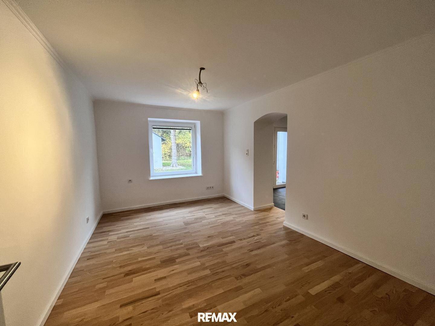 Helles Wohnzimmer mit Holzparkettboden und Fenster mit Blick ins Grüne.