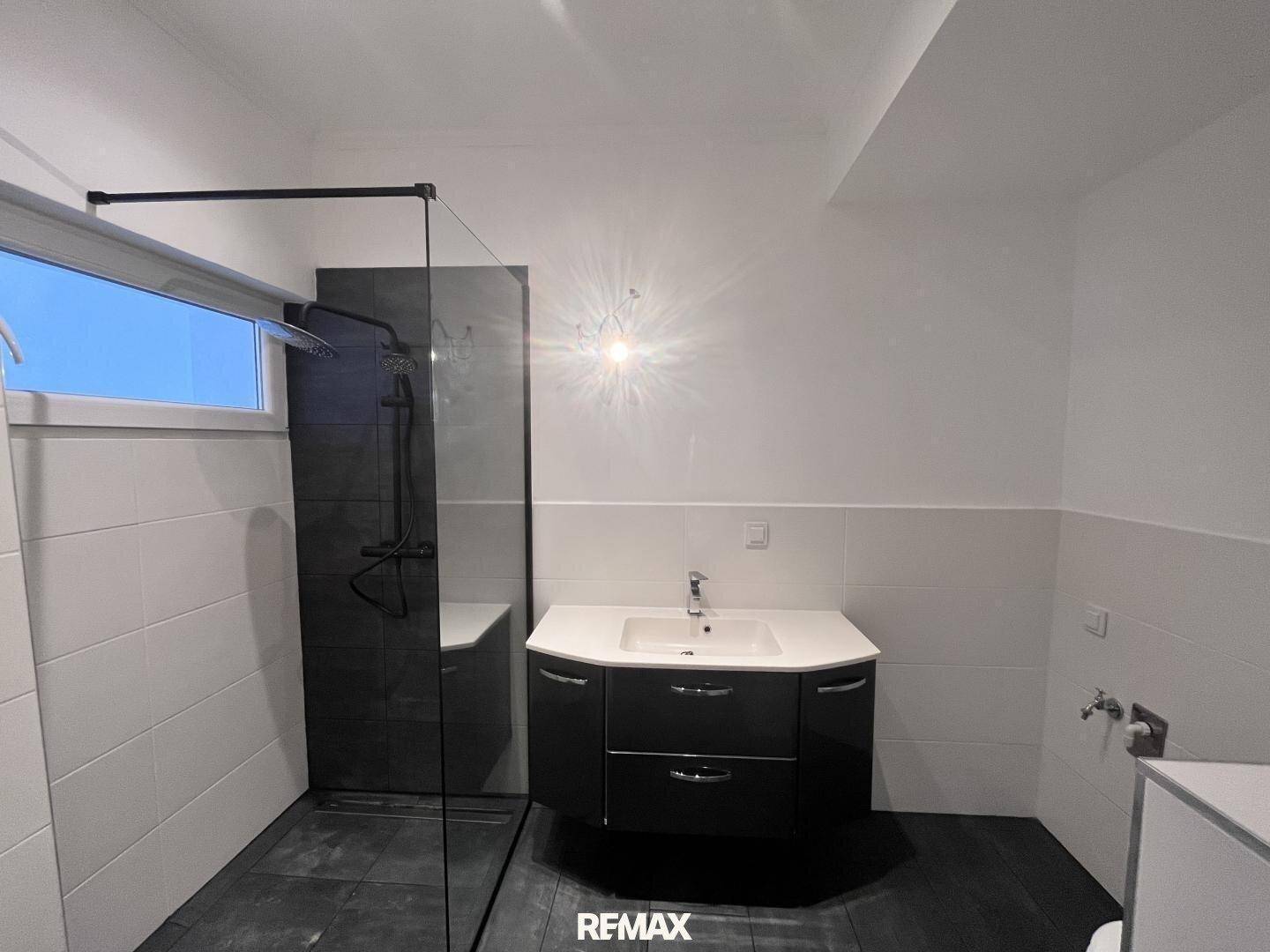 Helles Badezimmer mit begehbarer Dusche, modernem Waschtisch und Fenster.