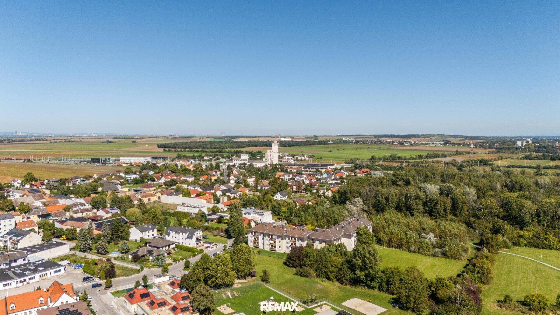 Weitläufige Luftaufnahme einer ländlichen Siedlung, umgeben von Feldern, Wäldern und weitem Himmel.