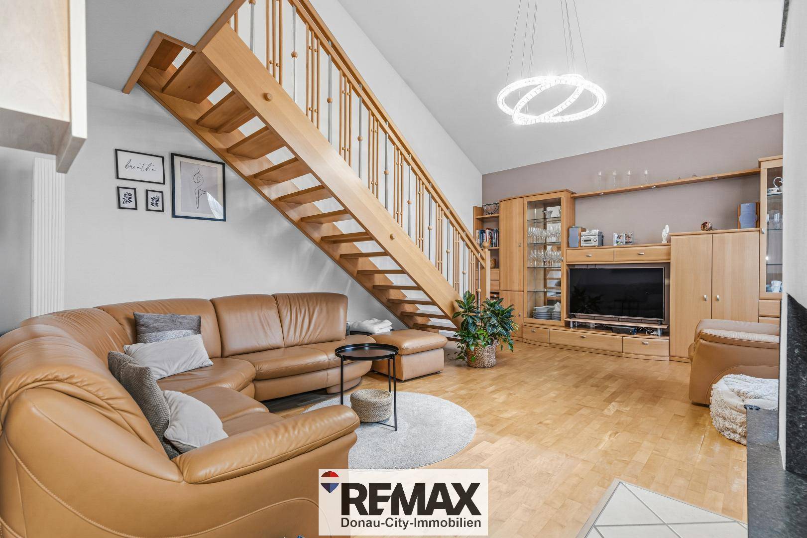 Geräumiges Wohnzimmer mit Ledersofa, Holztreppe zur Galerie und integrierten Holzmöbeln.
