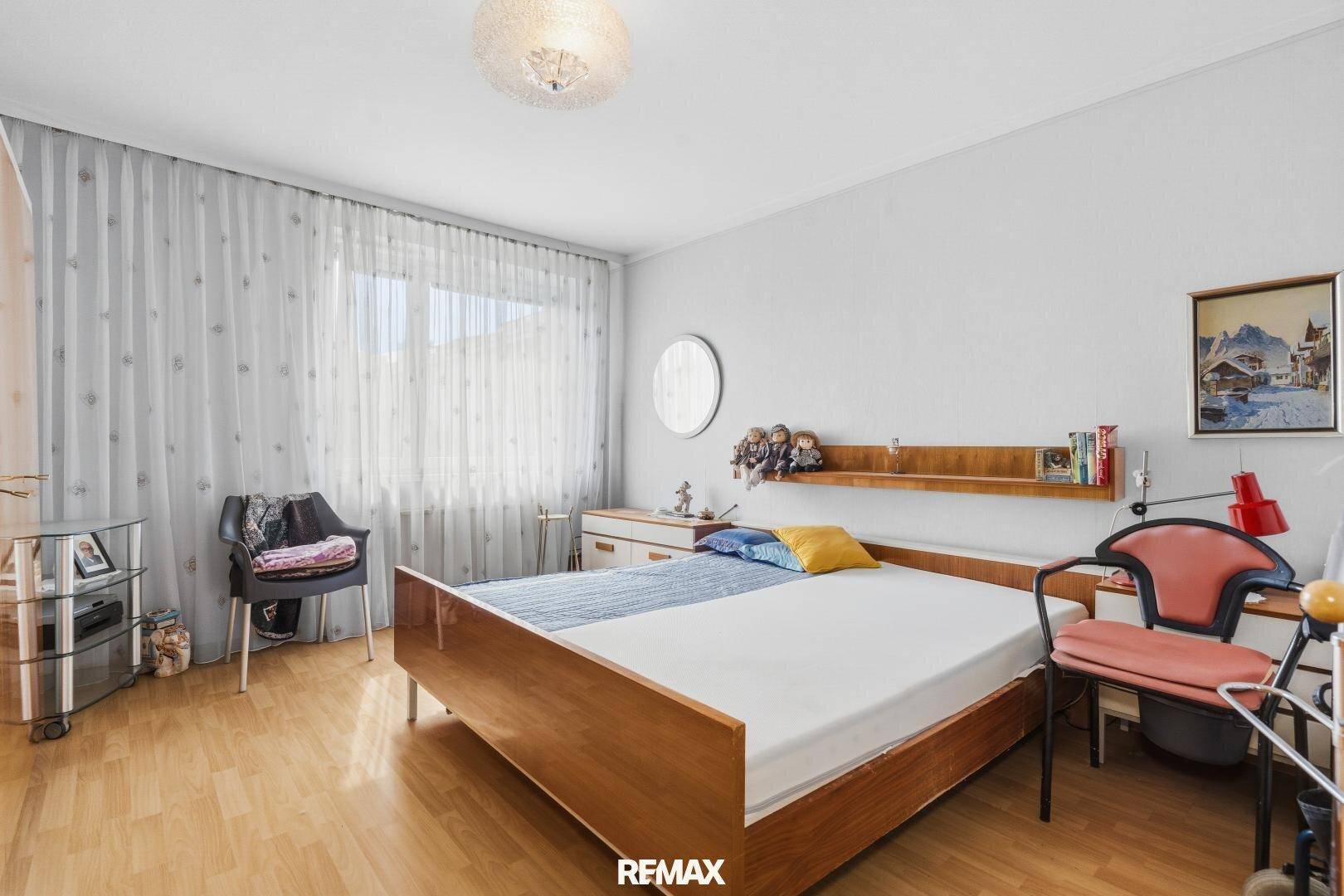 Schlafzimmer mit Holzbettrahmen, Laminatboden und großem Fenster mit Vorhängen.
