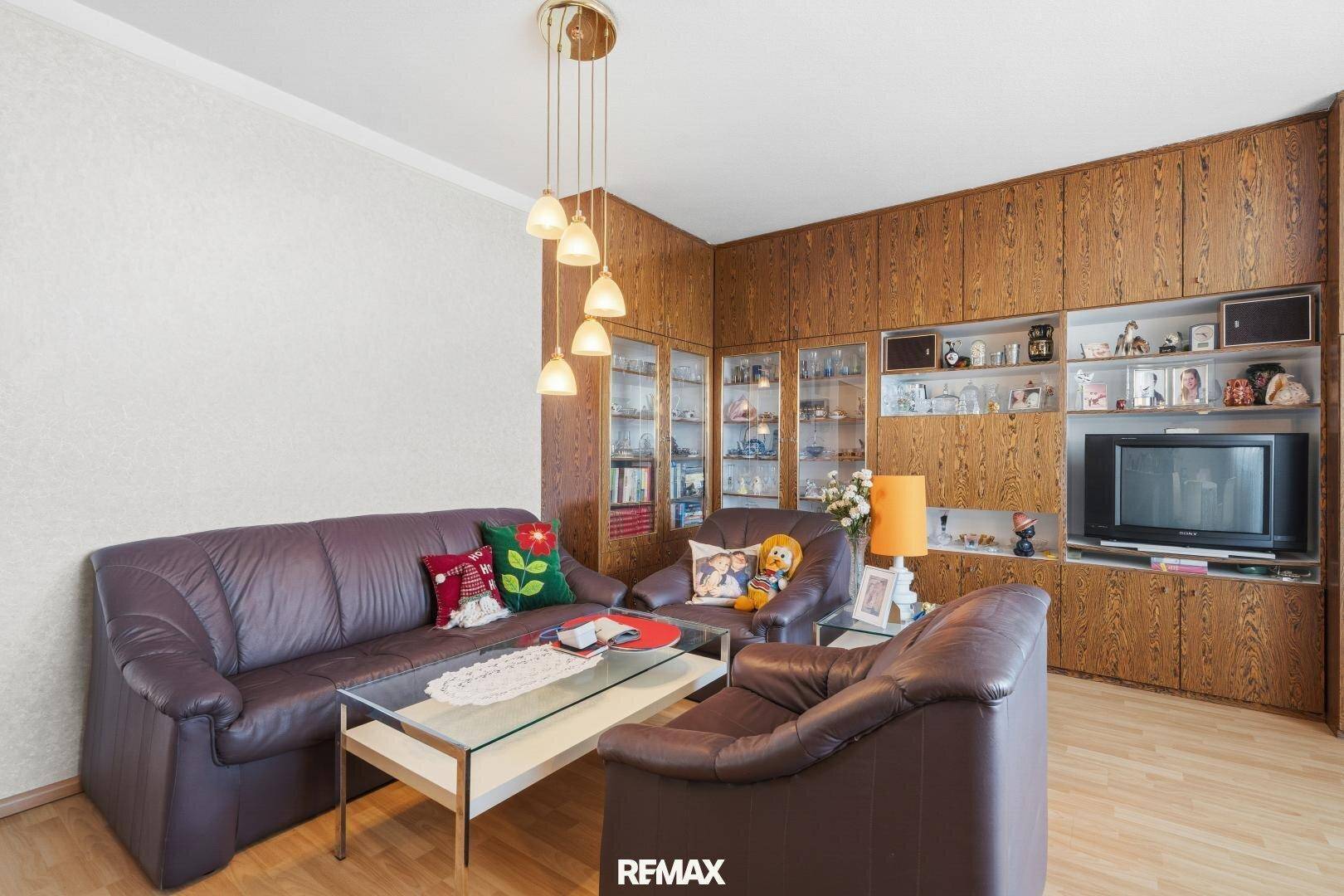 Wohnzimmer mit braunen Ledersofas, Holzschränken und einem Couchtisch.