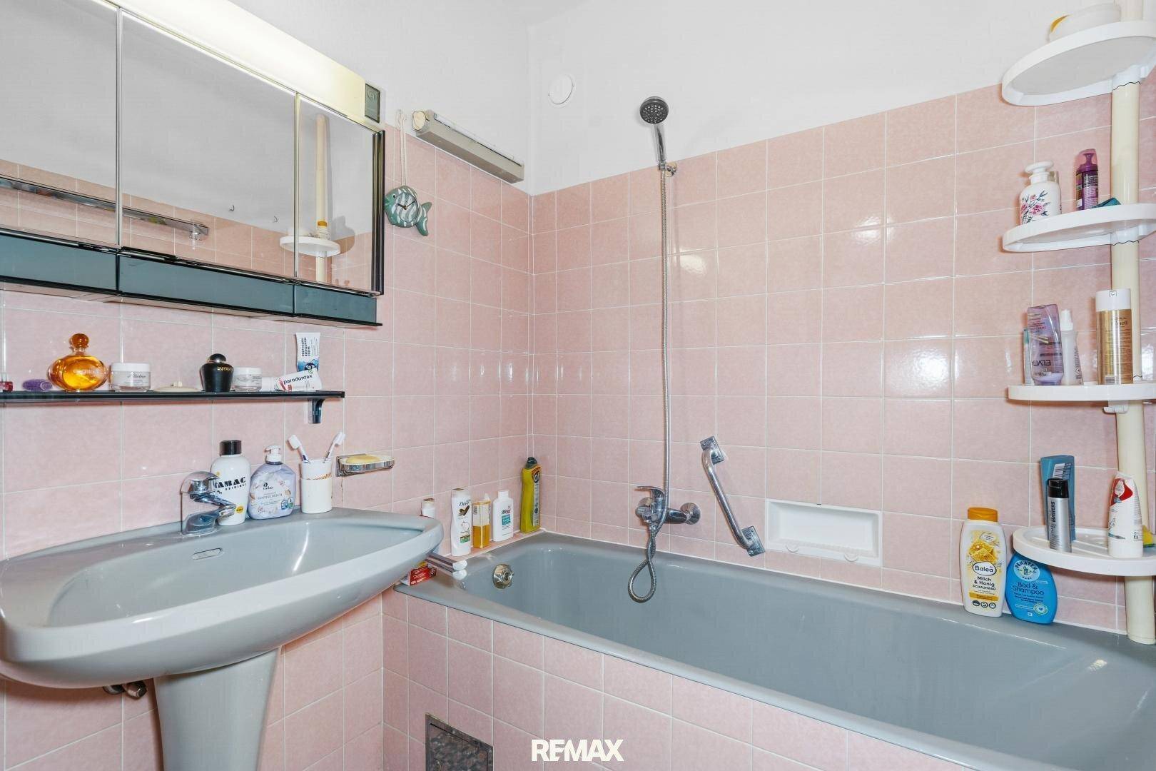 Badezimmer mit rosa Fliesen, Badewanne mit Duschfunktion und einem Waschbecken.