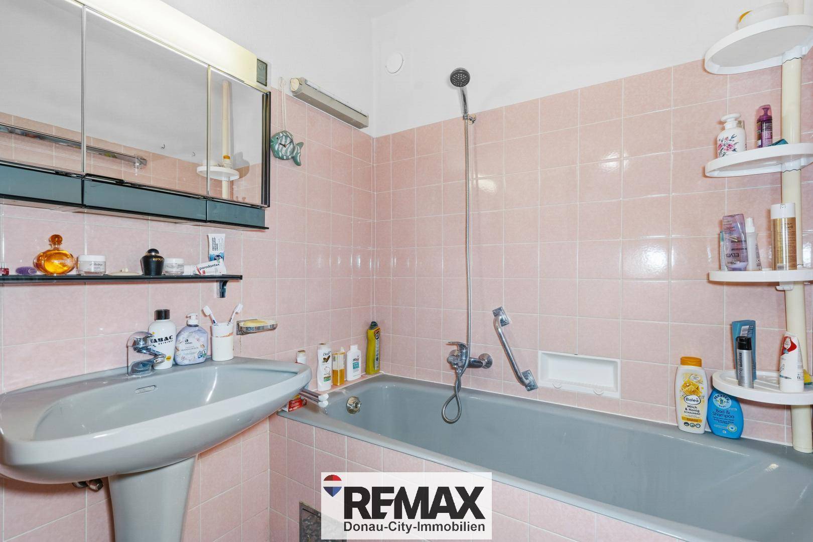 Badezimmer im Stil der 80er Jahre mit rosa Fliesen, Badewanne und Waschbecken.