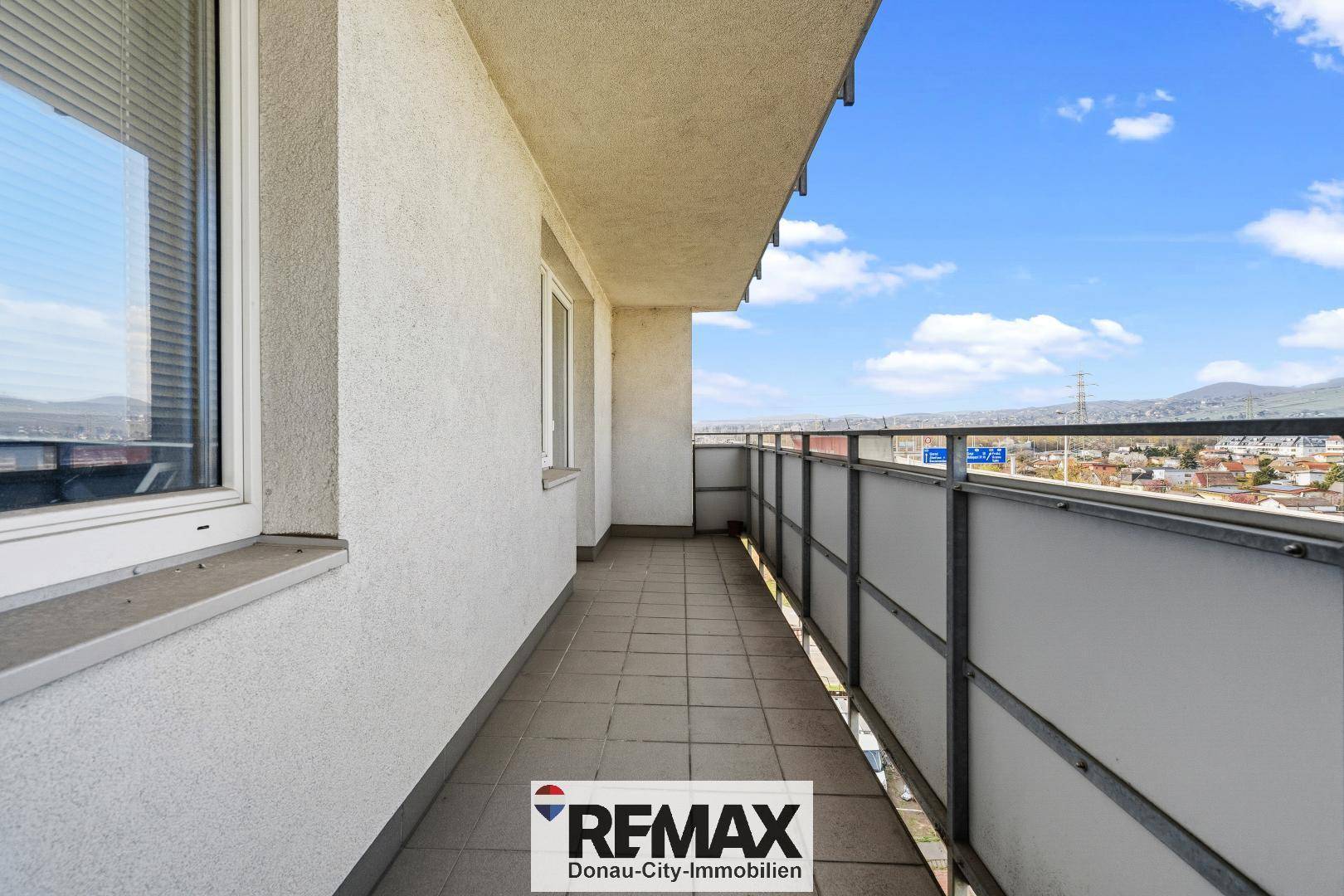 Langer Balkon mit Fliesenboden und Blick auf die umliegende Stadtlandschaft und Berge.