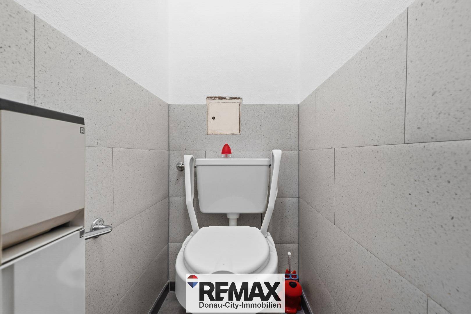 Kleines Gäste-WC mit grauen Fliesen und einer wandmontierten Toilette.
