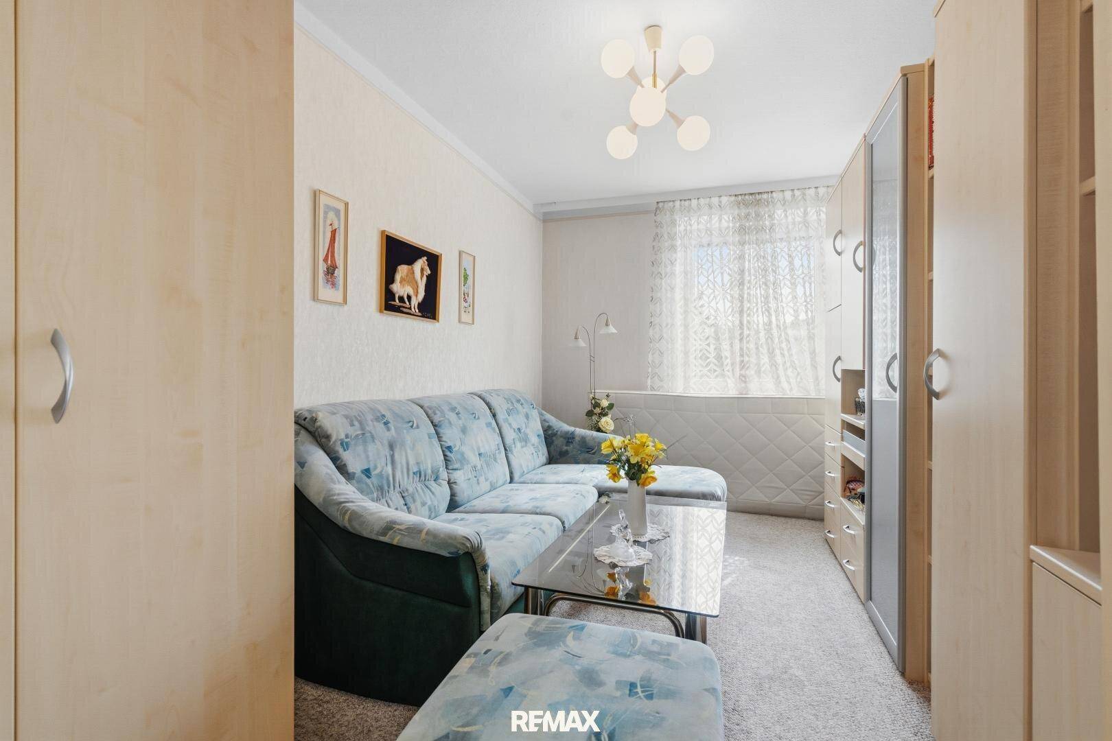 Kleines Zimmer mit blau gemustertem Sofa, Teppichboden und Einbauschränken.