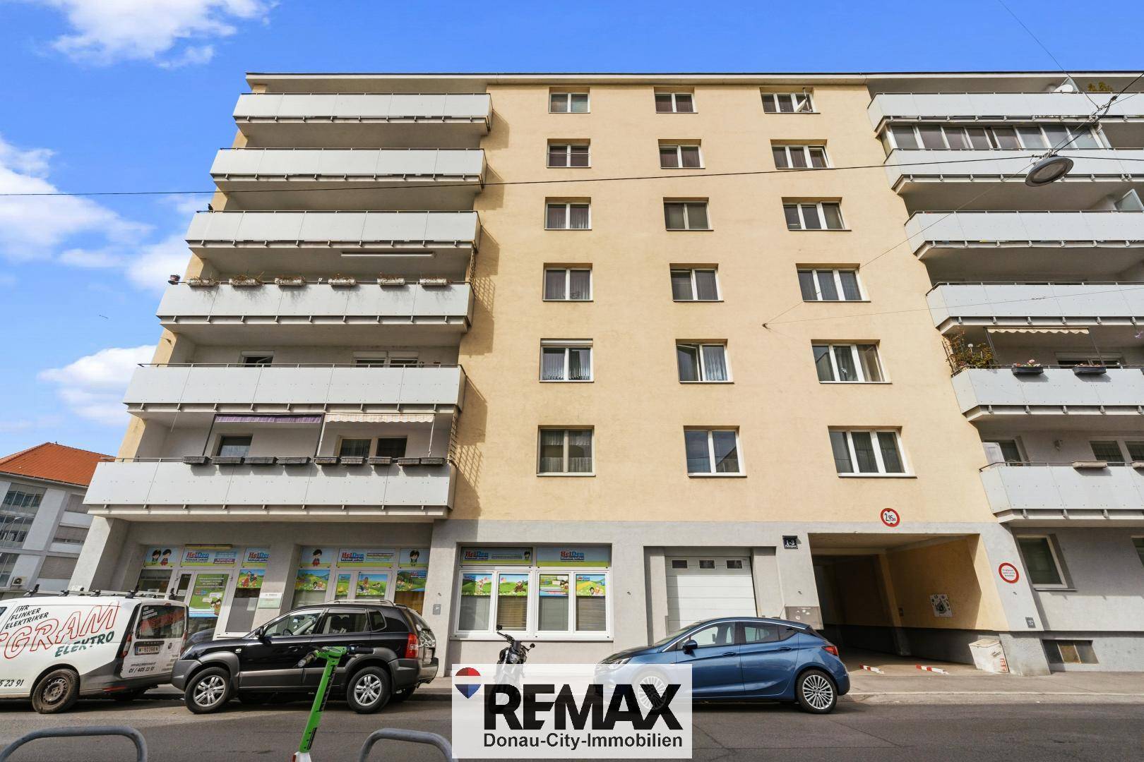 Fassade eines Mehrfamilienhauses mit zahlreichen Balkonen und Geschäften im Erdgeschoss.