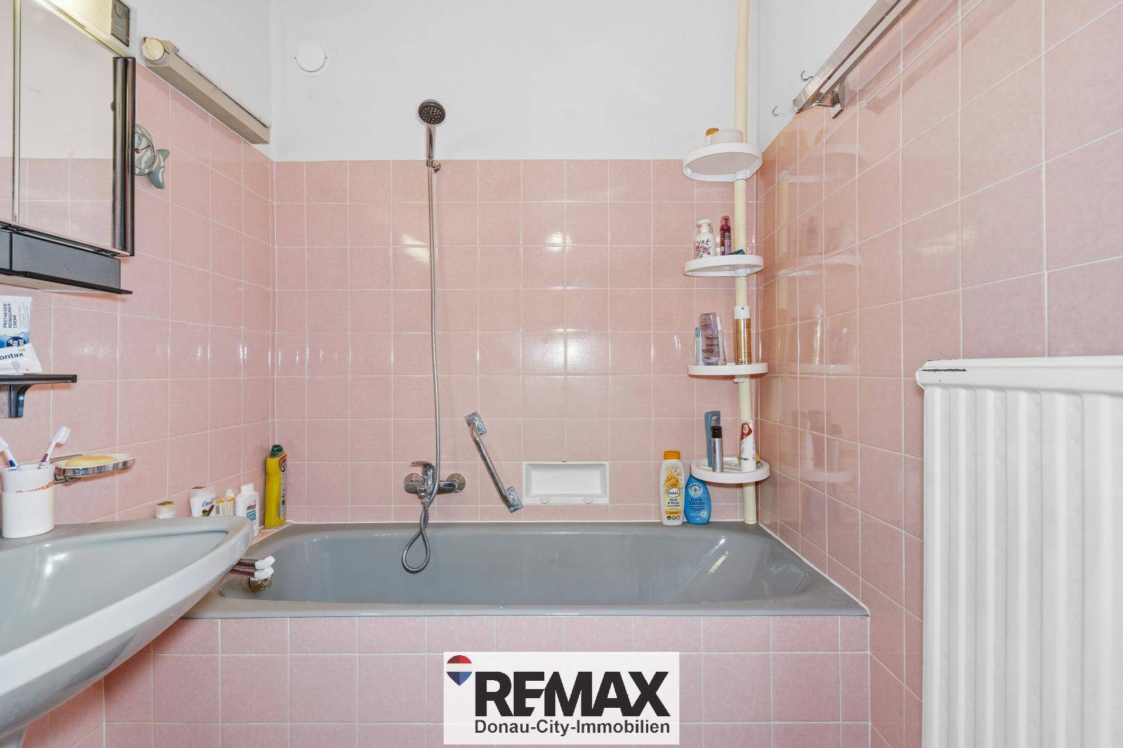 Badezimmer mit rosa Wandfliesen, einer Badewanne mit Duschfunktion und einem Heizkörper.