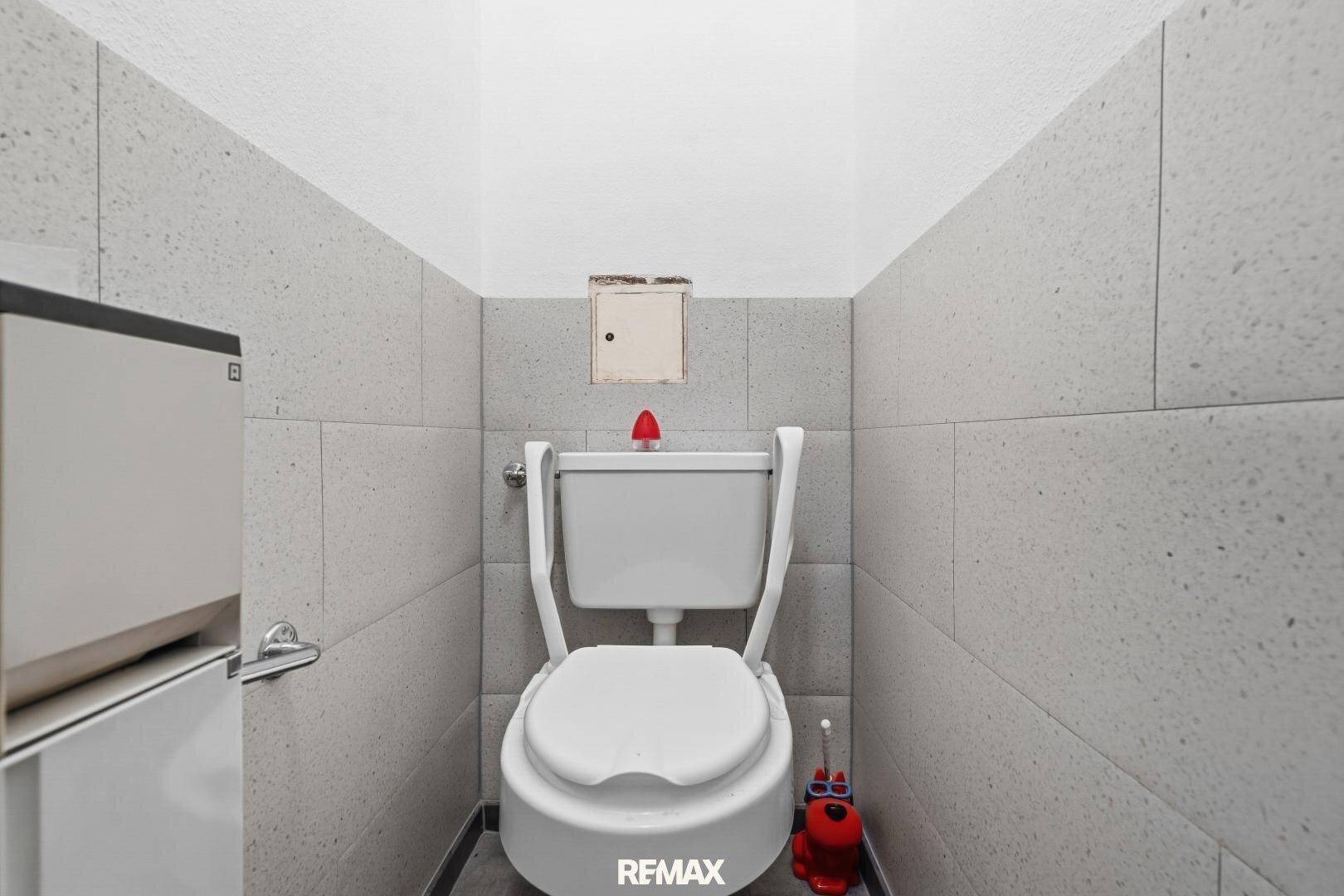 Kleines WC mit hellgrauen Fliesen an den Wänden und einer weißen Toilette.