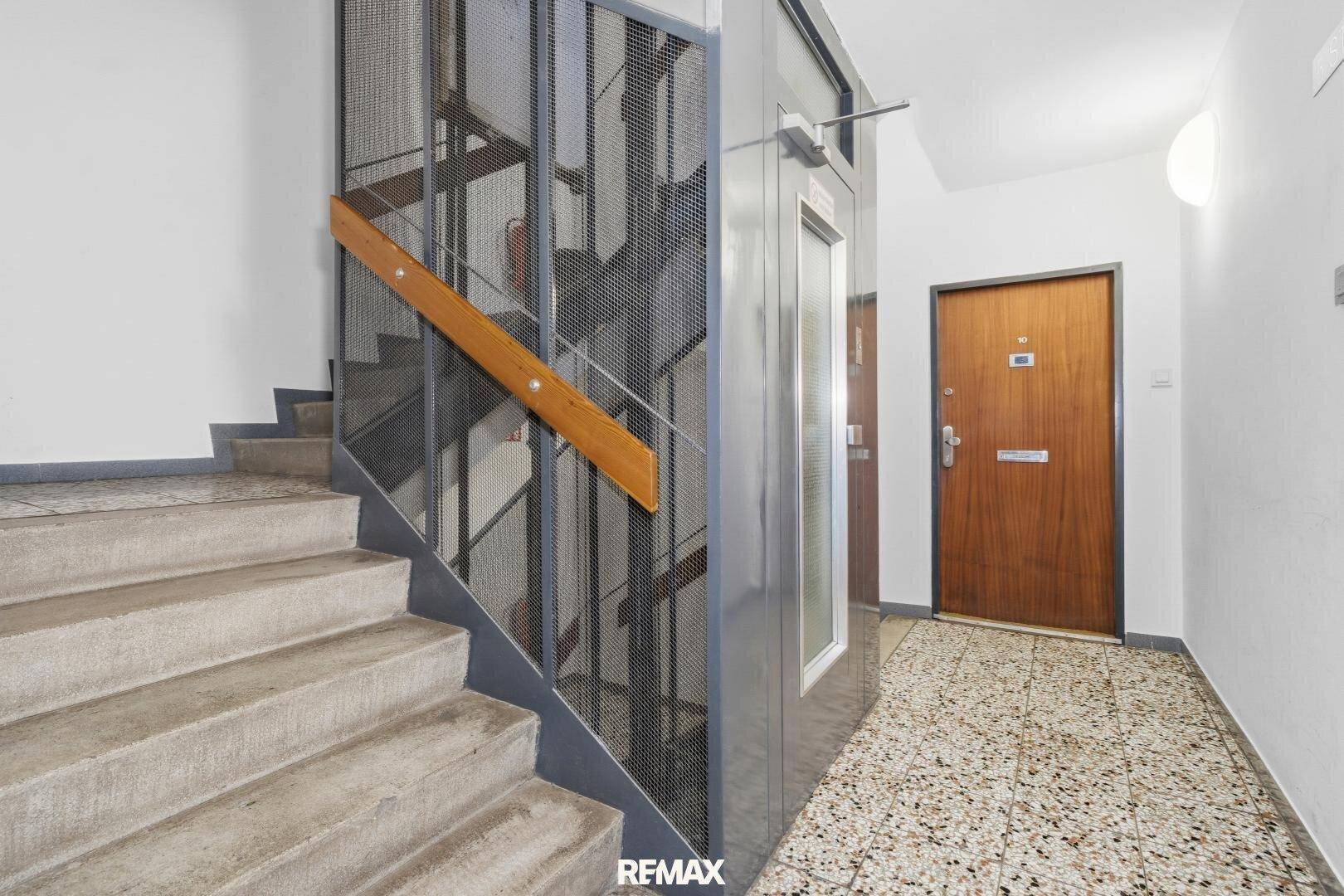 Treppenhaus mit Betontreppen, Gitteraufzug und Holzhandlauf.