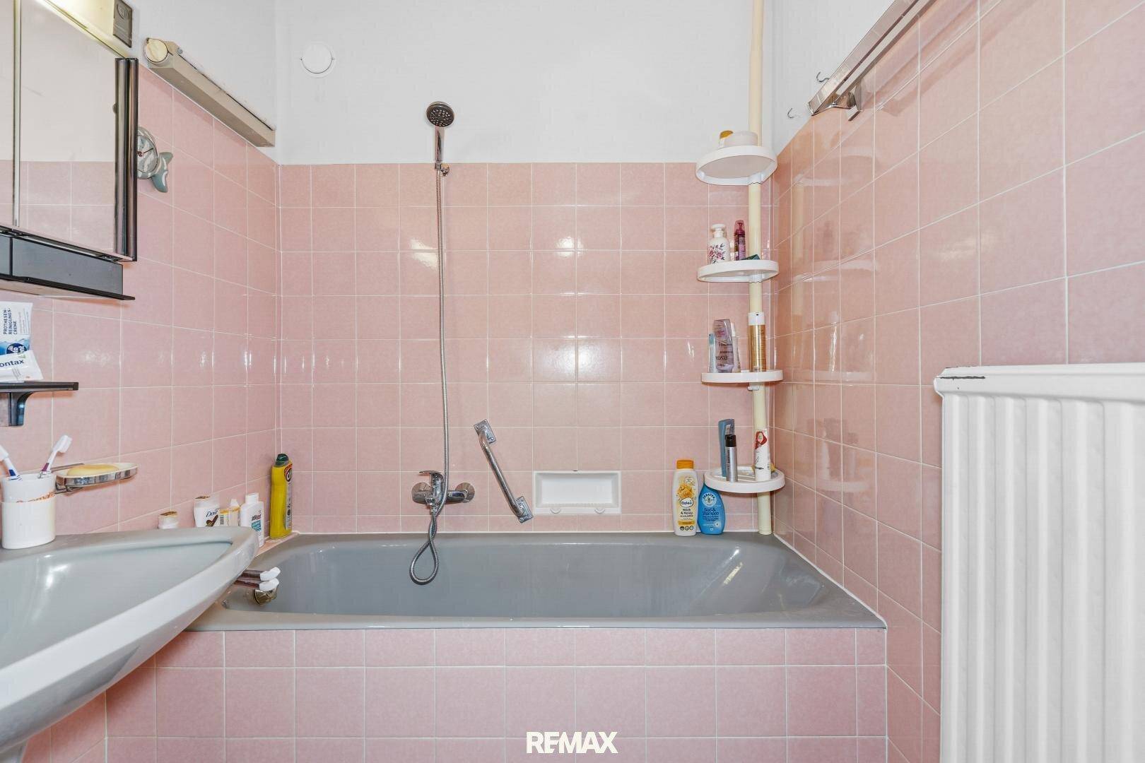 Badezimmer mit Badewanne, rosa Fliesen und einem Heizkörper.