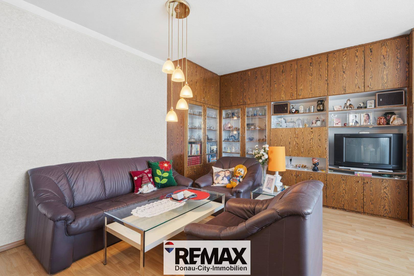 Wohnzimmer mit dunklen Ledersofas, Holzvertäfelung und einem Couchtisch aus Glas.