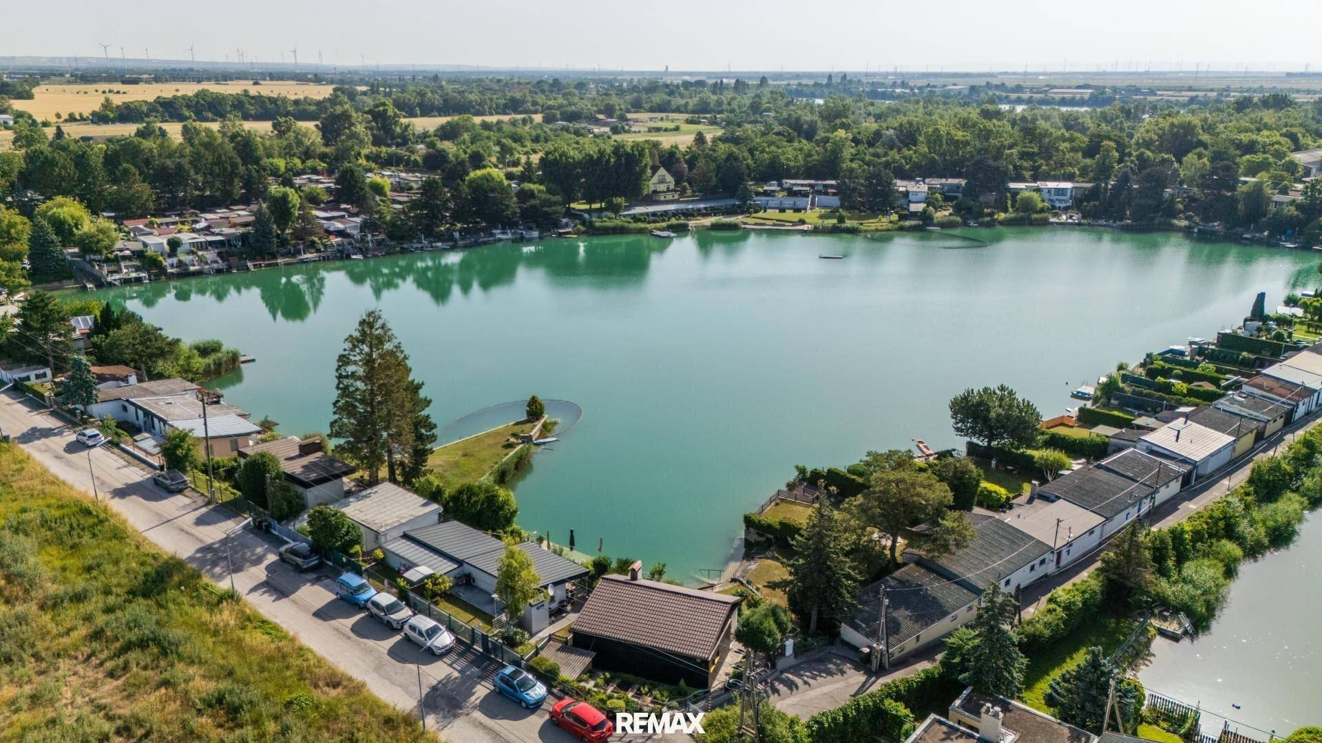 Luftaufnahme des Sees mit umliegenden Ferienhäusern und grüner Landschaft.