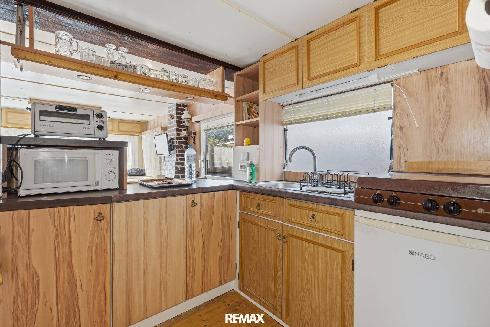 Kleine Küche mit Holzschränken, Spüle, Kühlschrank und Mikrowelle in funktionalem Design.