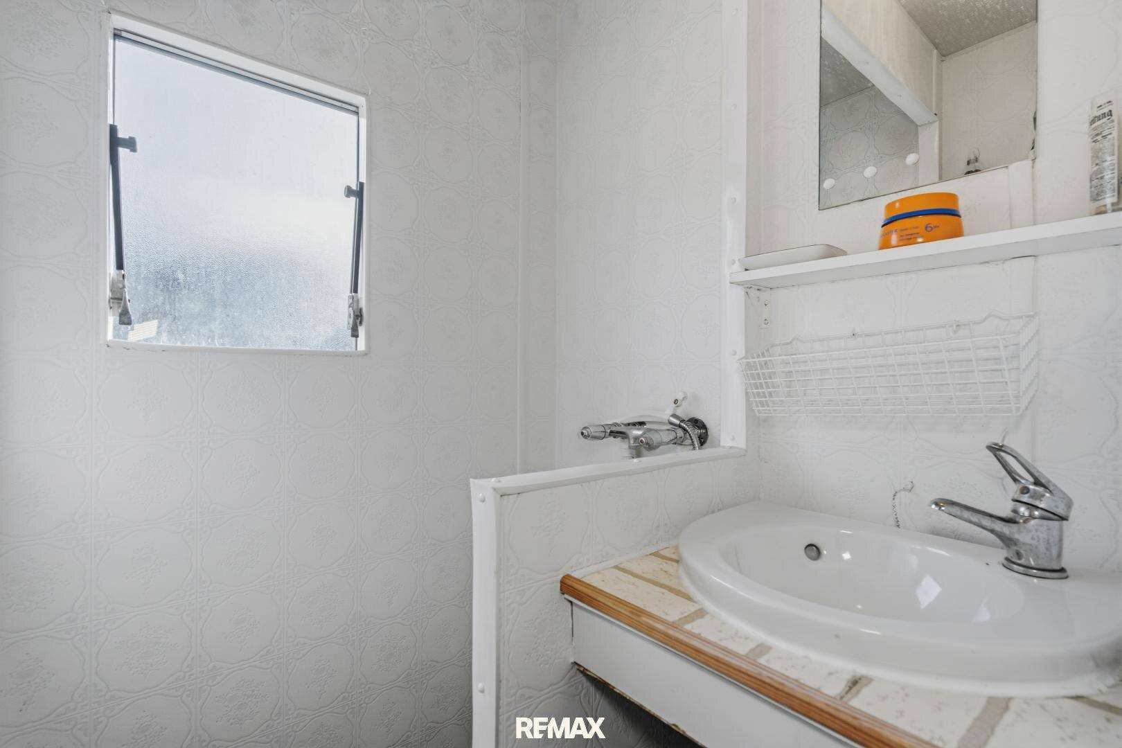 Kleines Badezimmer mit Waschbecken, Spiegel und einem Fenster für natürliche Belüftung.