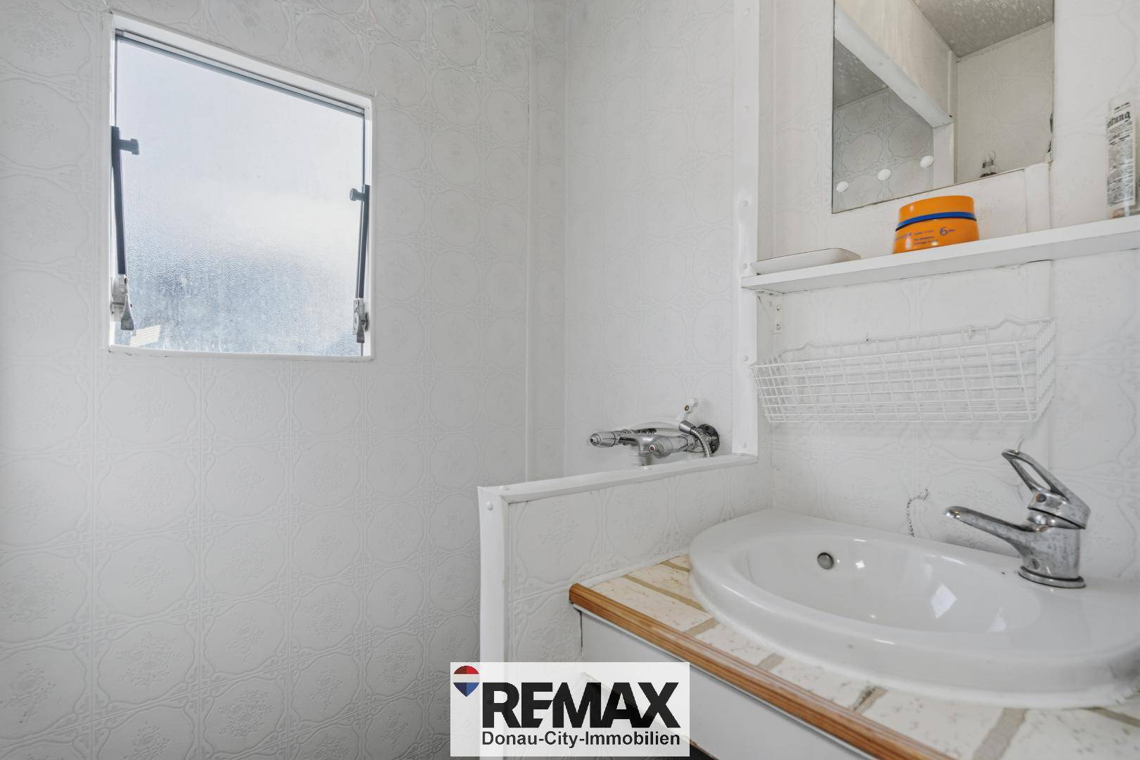 Kleines Badezimmer mit Einzelwaschbecken, Spiegel und einem Fenster für natürliche Belüftung.