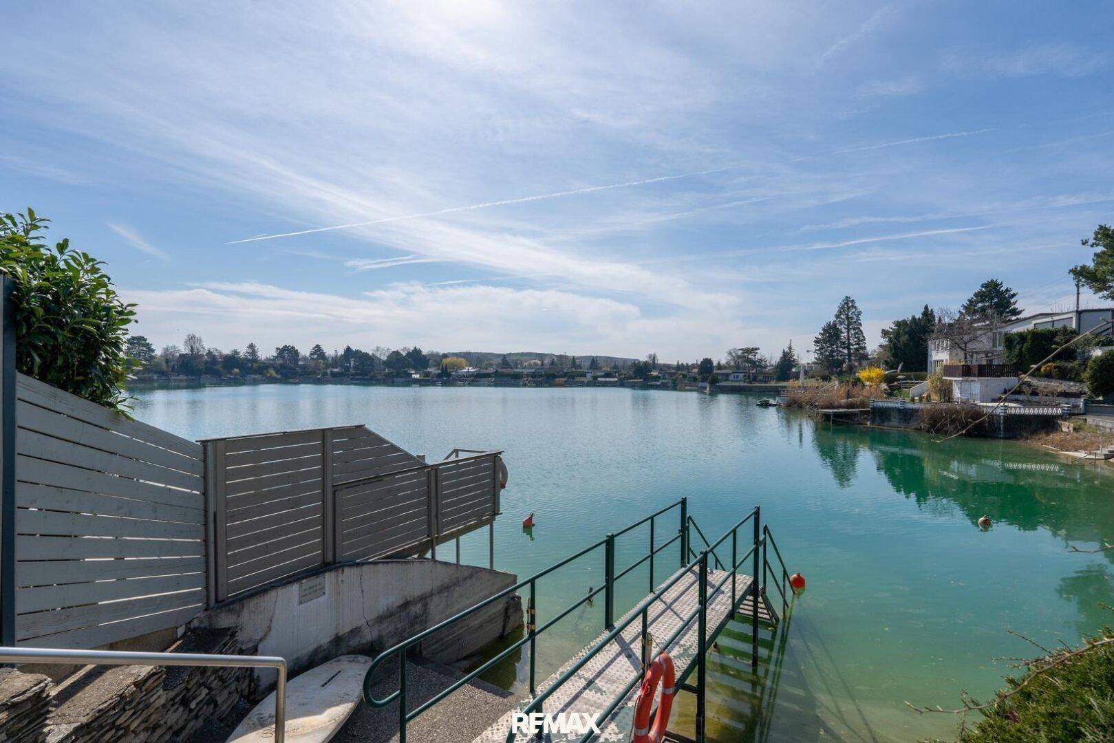 Malerischer See mit Steg und Zugang zum Wasser unter strahlend blauem Himmel.