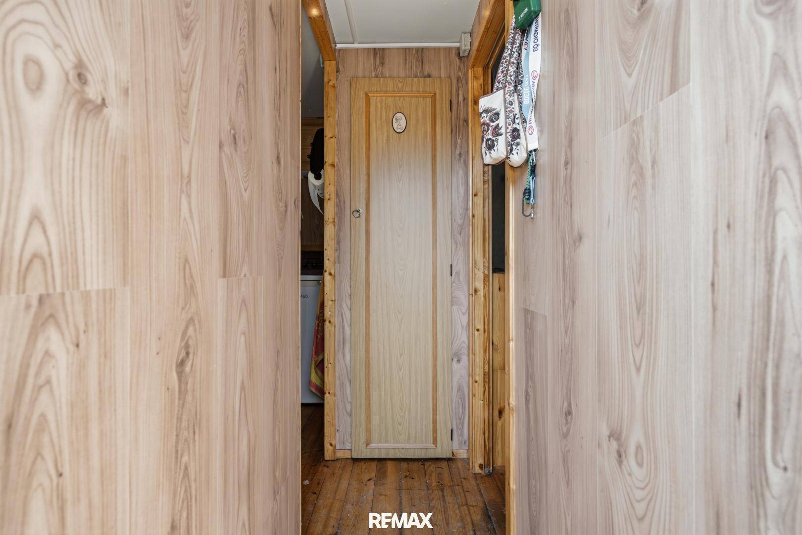 Schmaler Flur mit Holzverkleidung an den Wänden und einer einfachen Holztür.