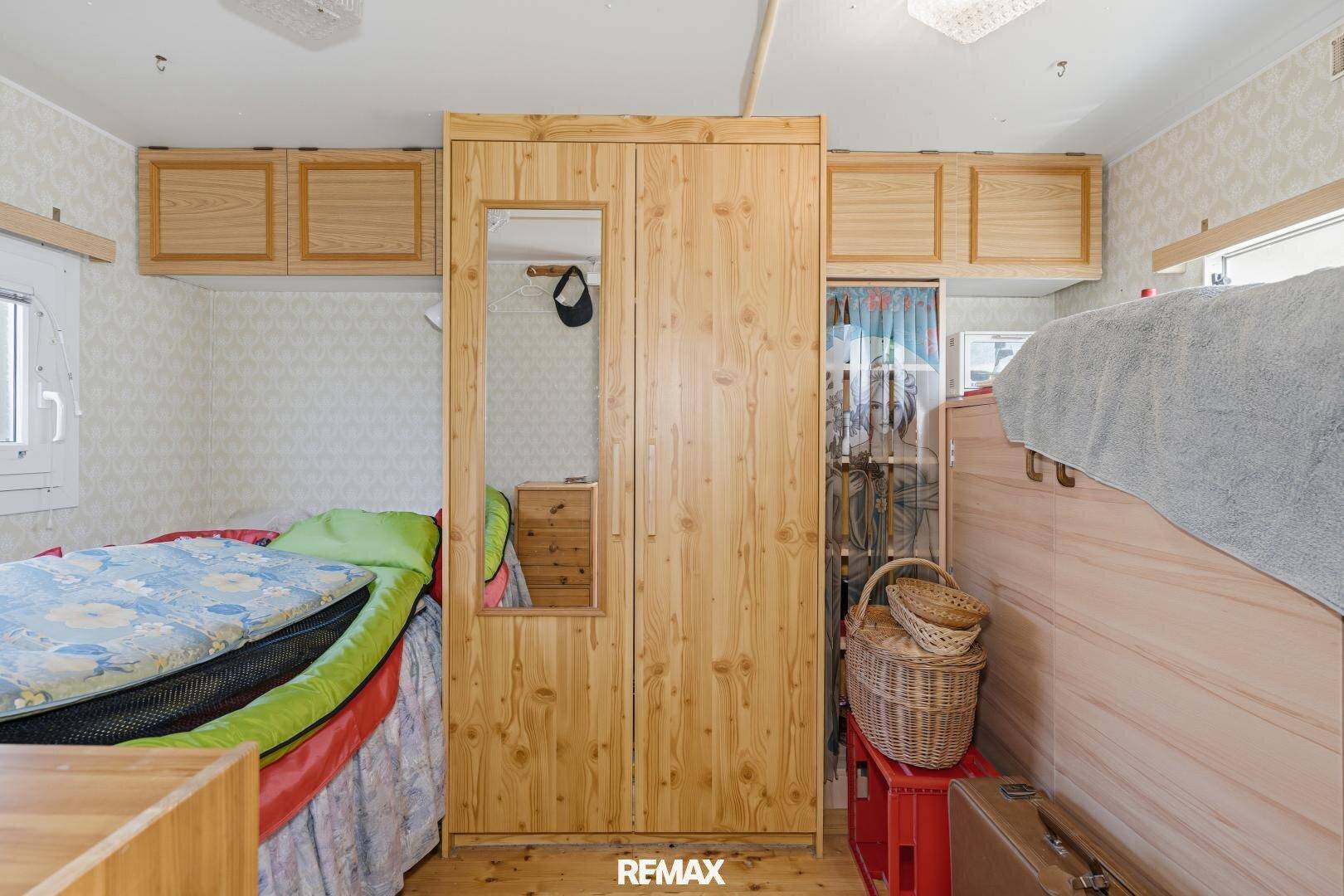Schlafzimmer mit Einzelbett, Holzschrank mit Spiegel und praktischen Oberschränken für Stauraum.