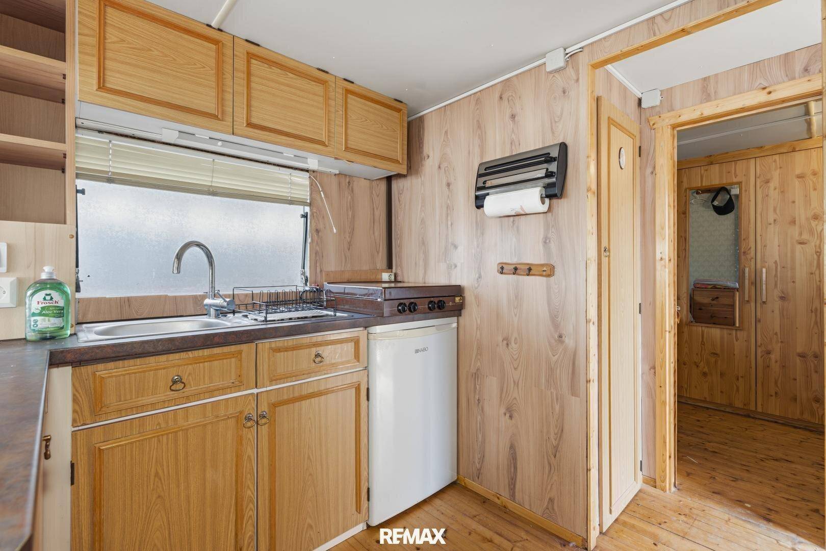 Funktionale Küchenzeile mit Holzfronten, Spülbecken und kleinem Kühlschrank für den täglichen Gebrauch.