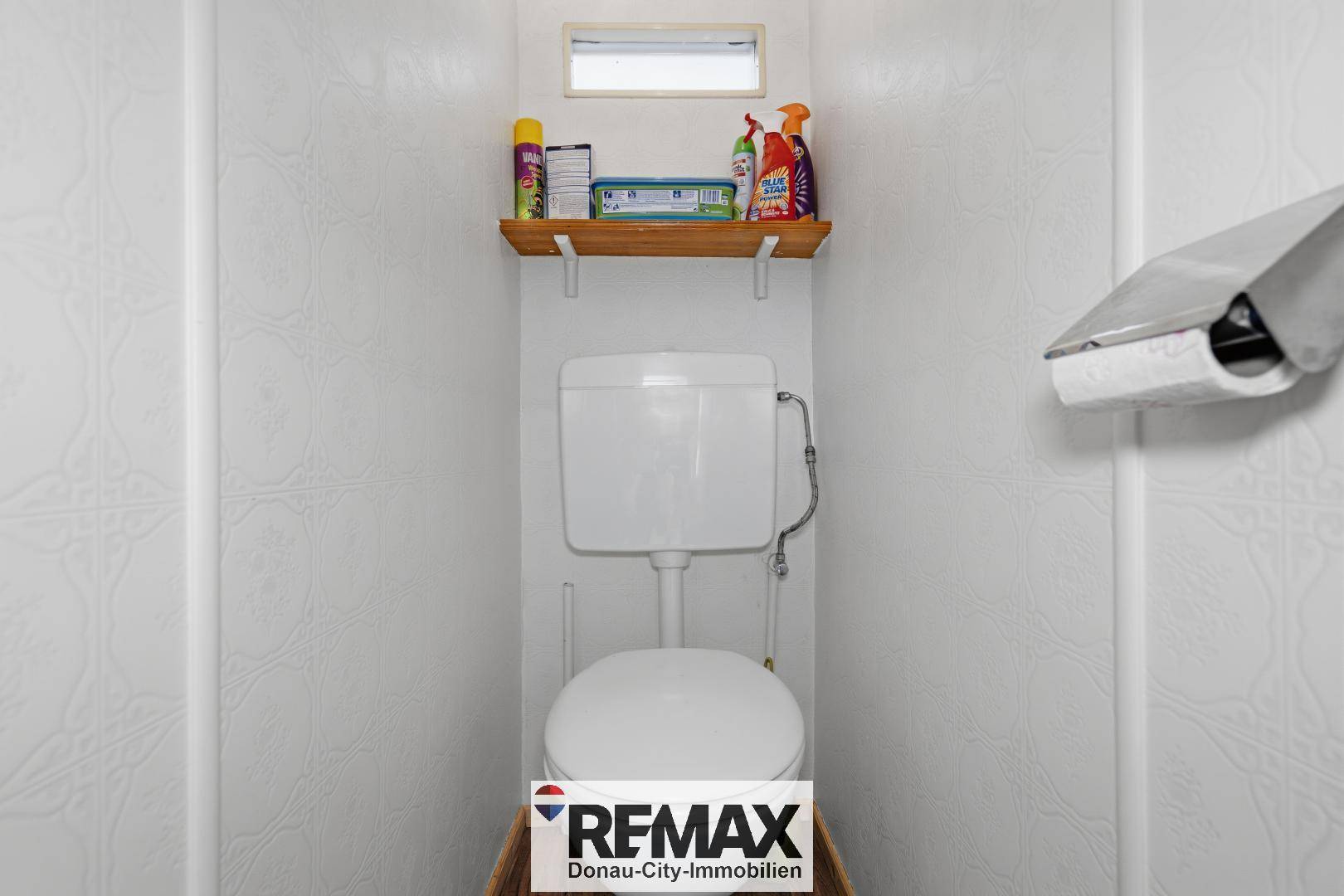 Separate Toilette mit WC, kleiner Ablage und einem kleinen Fenster.