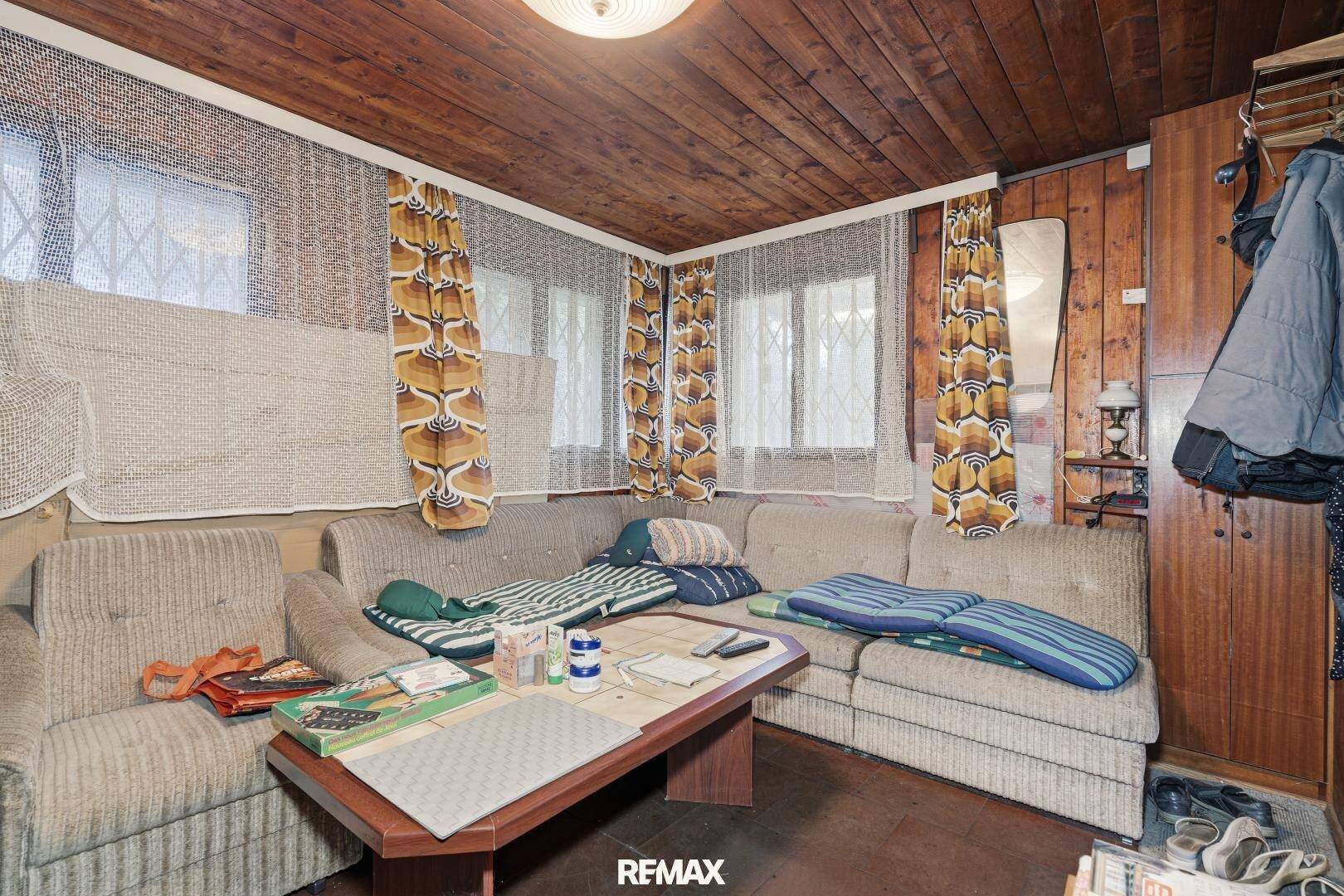 Gemütliches Wohnzimmer mit Holzdecke, bequemen Sofas und Fenstern mit gemusterten Vorhängen.