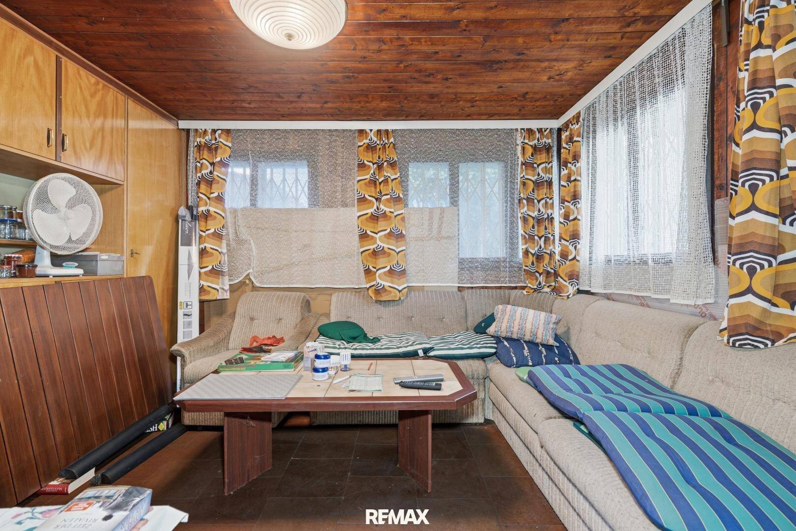 Wohnzimmer mit Holzdecke, Einbauschränken und Sitzgelegenheiten in einem älteren Stil.