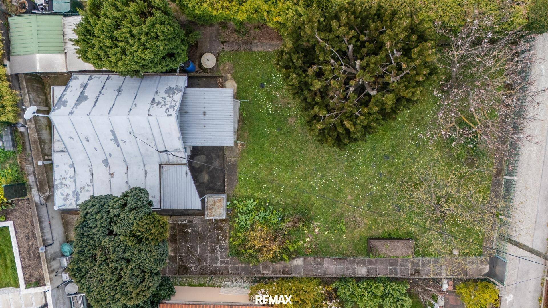 Luftaufnahme des Grundstücks mit kleinem Haus, Garten und umliegenden Bäumen.