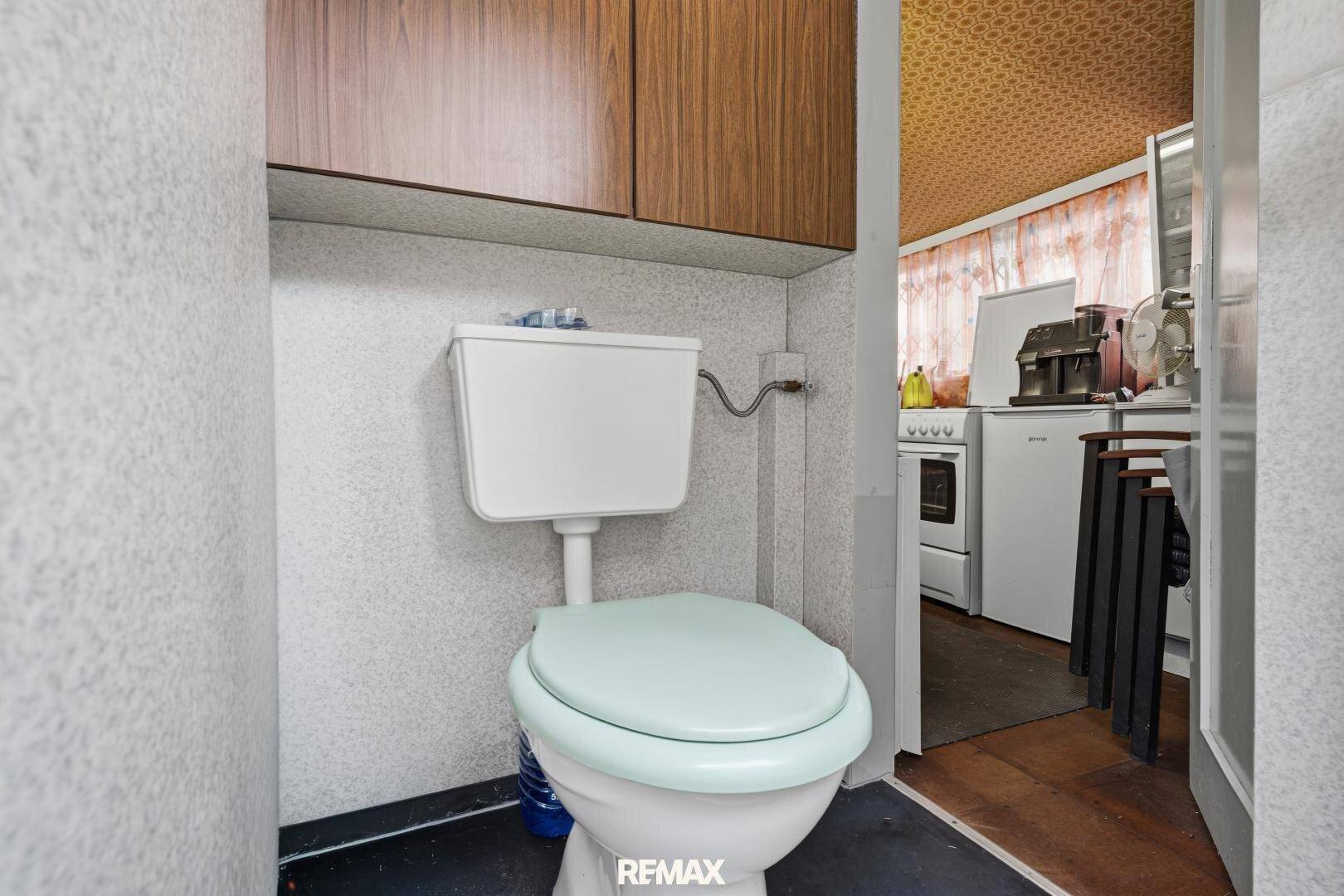 Kleines WC mit einfacher Toilette und schlichten Wänden, angrenzend an die Küche.