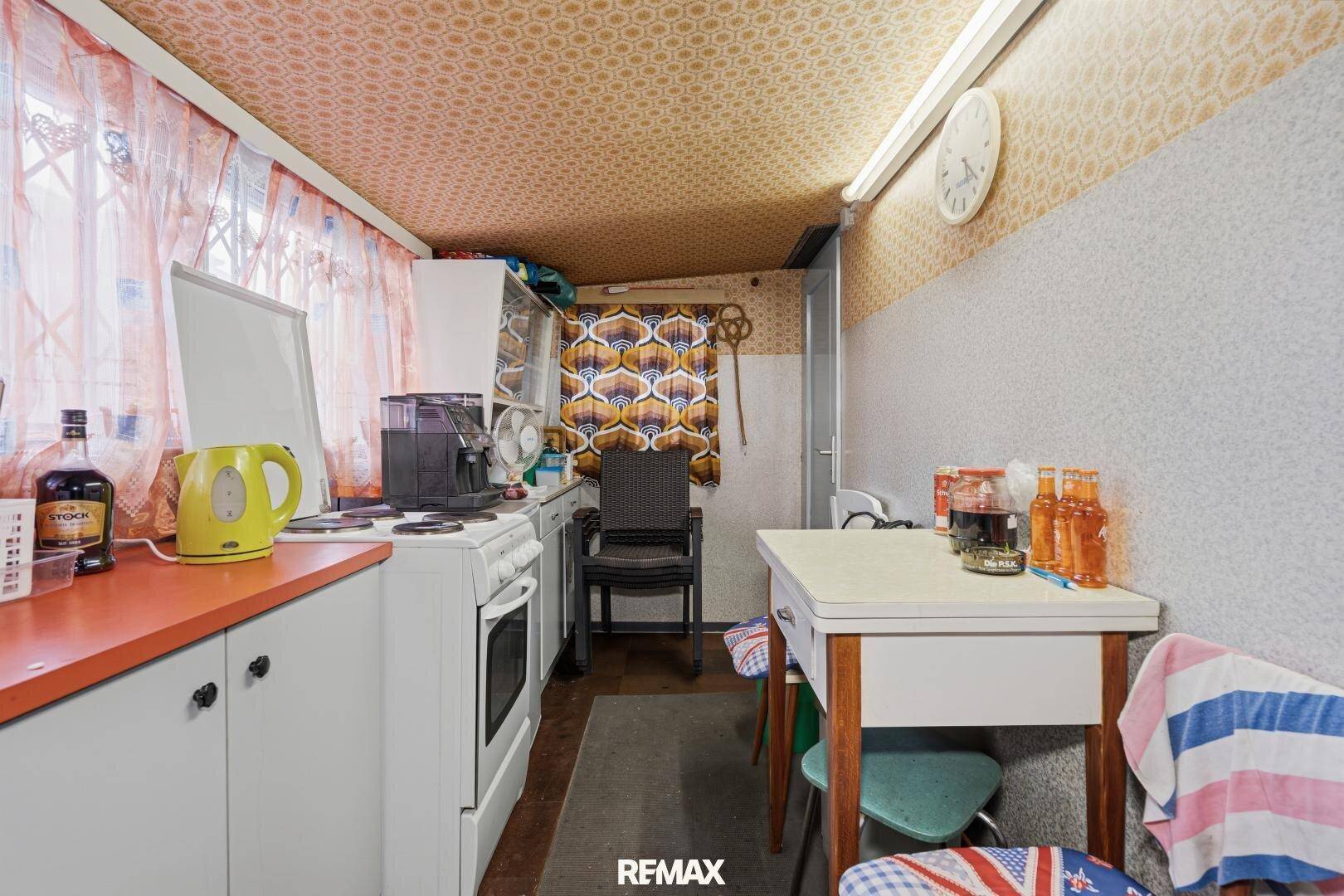 Schmale Küche mit Esstisch, einfacher Einrichtung und gemusterter Tapete an der Decke.