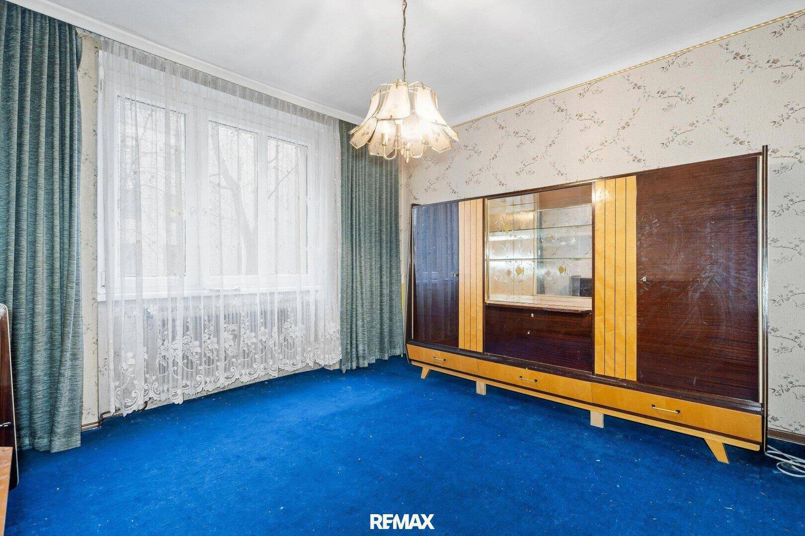 Schlafzimmer im Vintage-Stil mit blauem Teppich, gemusterter Tapete und einem großen Fenster.