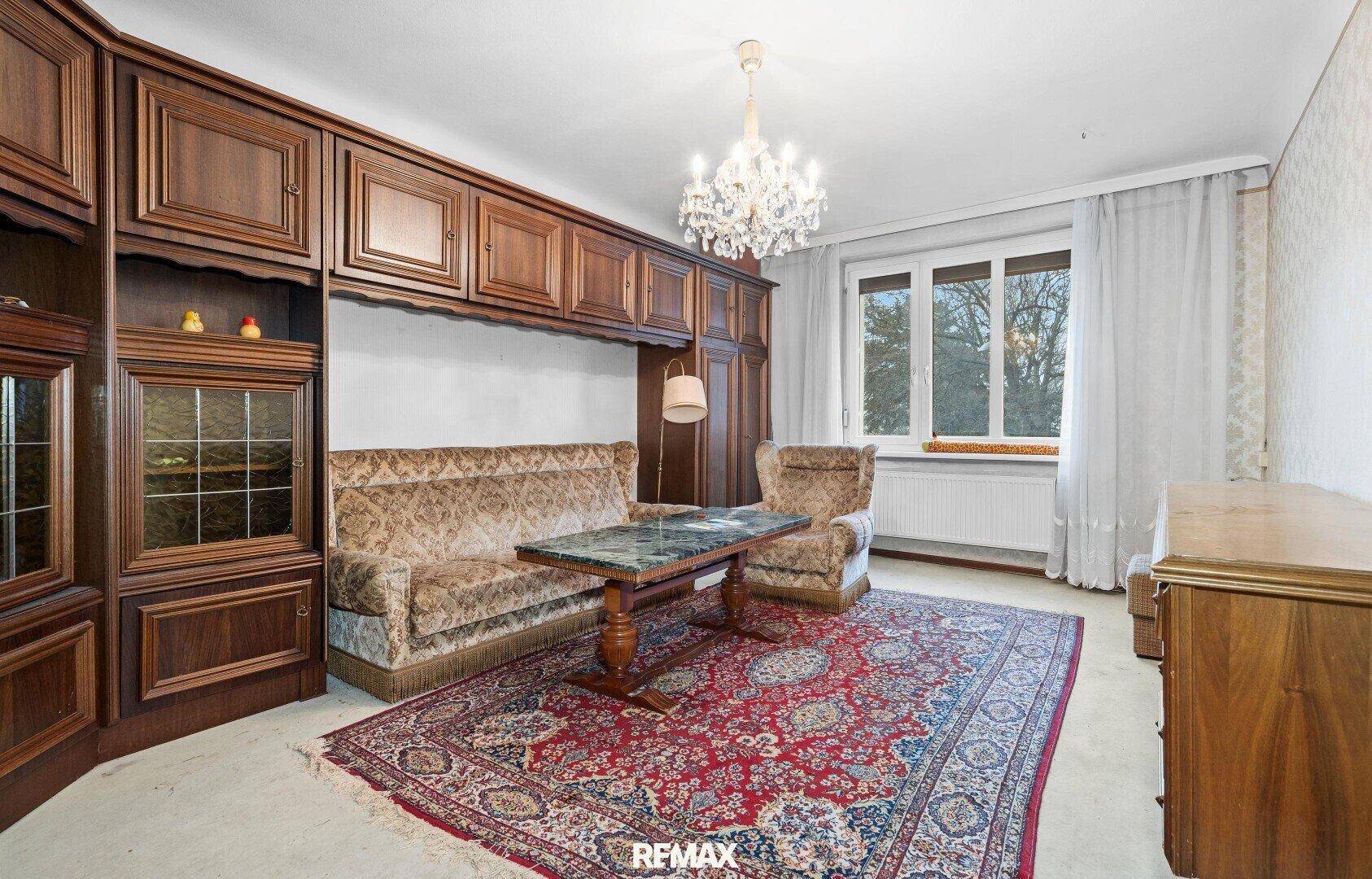 Klassisches Wohnzimmer mit dunklen Holzschränken, Teppich und einem großen Fenster mit Vorhängen.