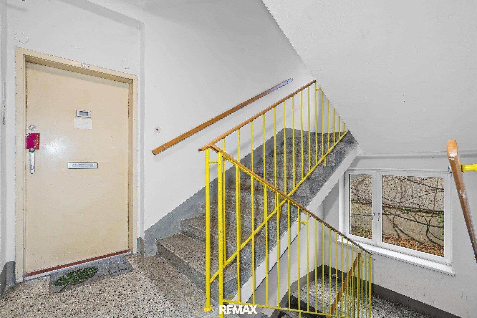 Treppenhaus mit gelbem Geländer und Terrazzoboden, das zu den oberen Etagen führt.