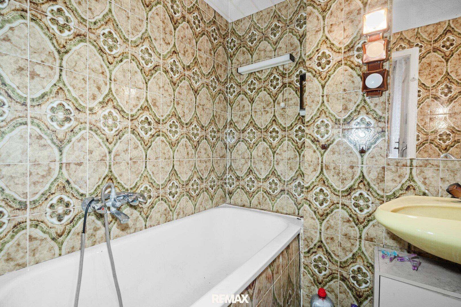 Badezimmer mit Badewanne und auffälligen gemusterten Fliesen im Stil der 80er Jahre.