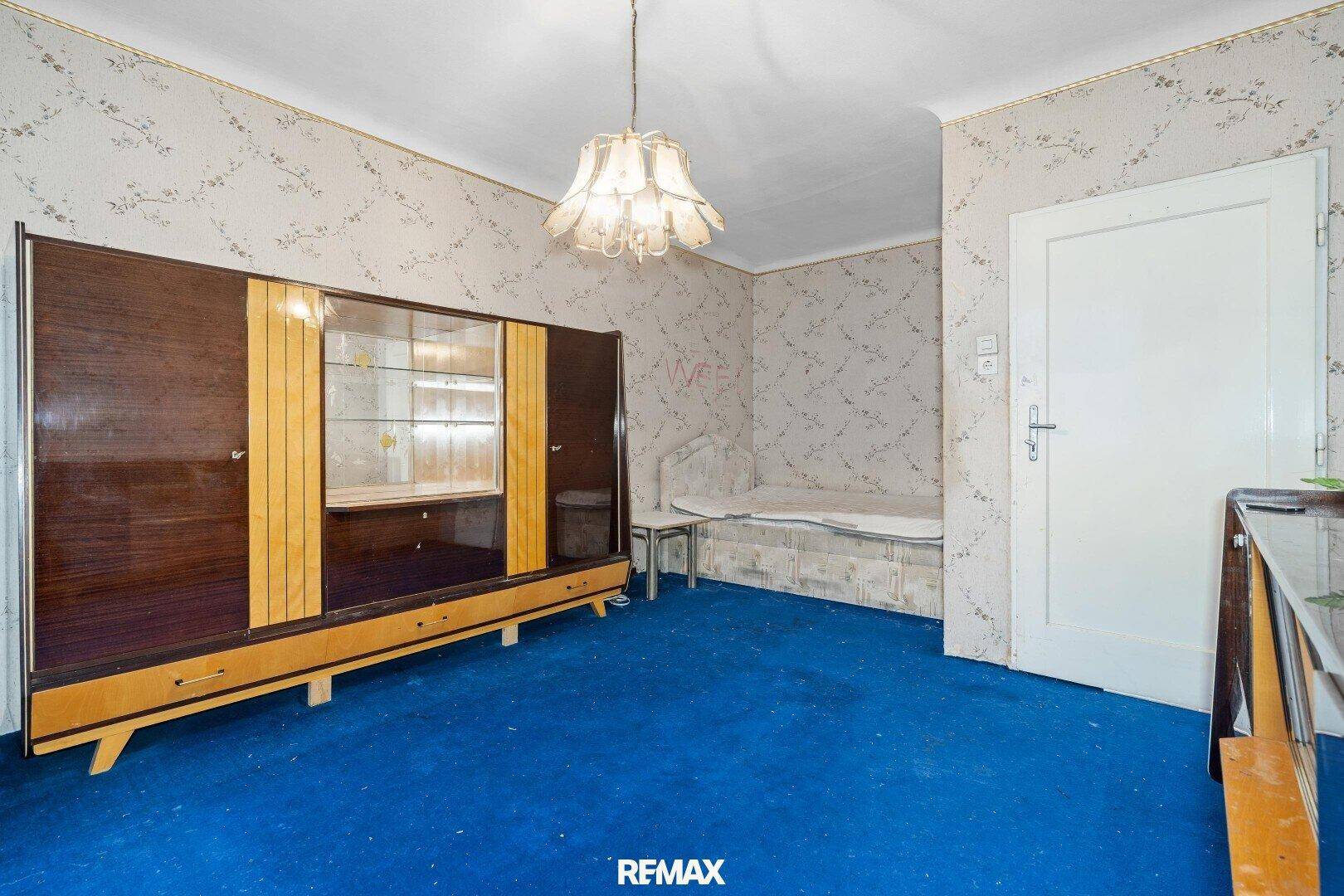Schlafzimmer mit blauem Teppich, gemusterter Tapete und einem großen Schrank im Retro-Stil.