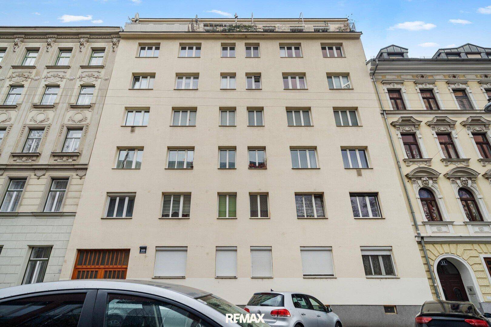 Fassade eines Mehrfamilienhauses mit vielen Fenstern und geparkten Autos davor.